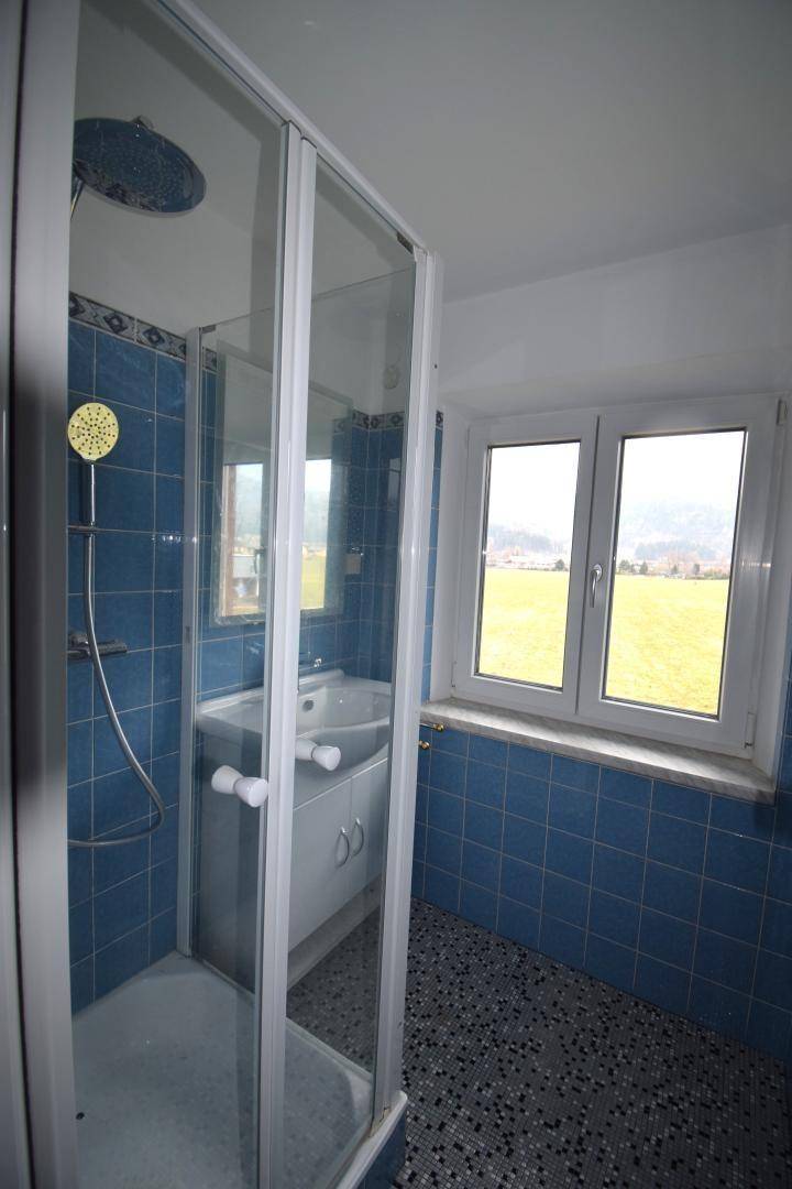 Badezimmer mit blauen Fliesen, Duschkabine und einem Fenster mit Blick ins Grüne.