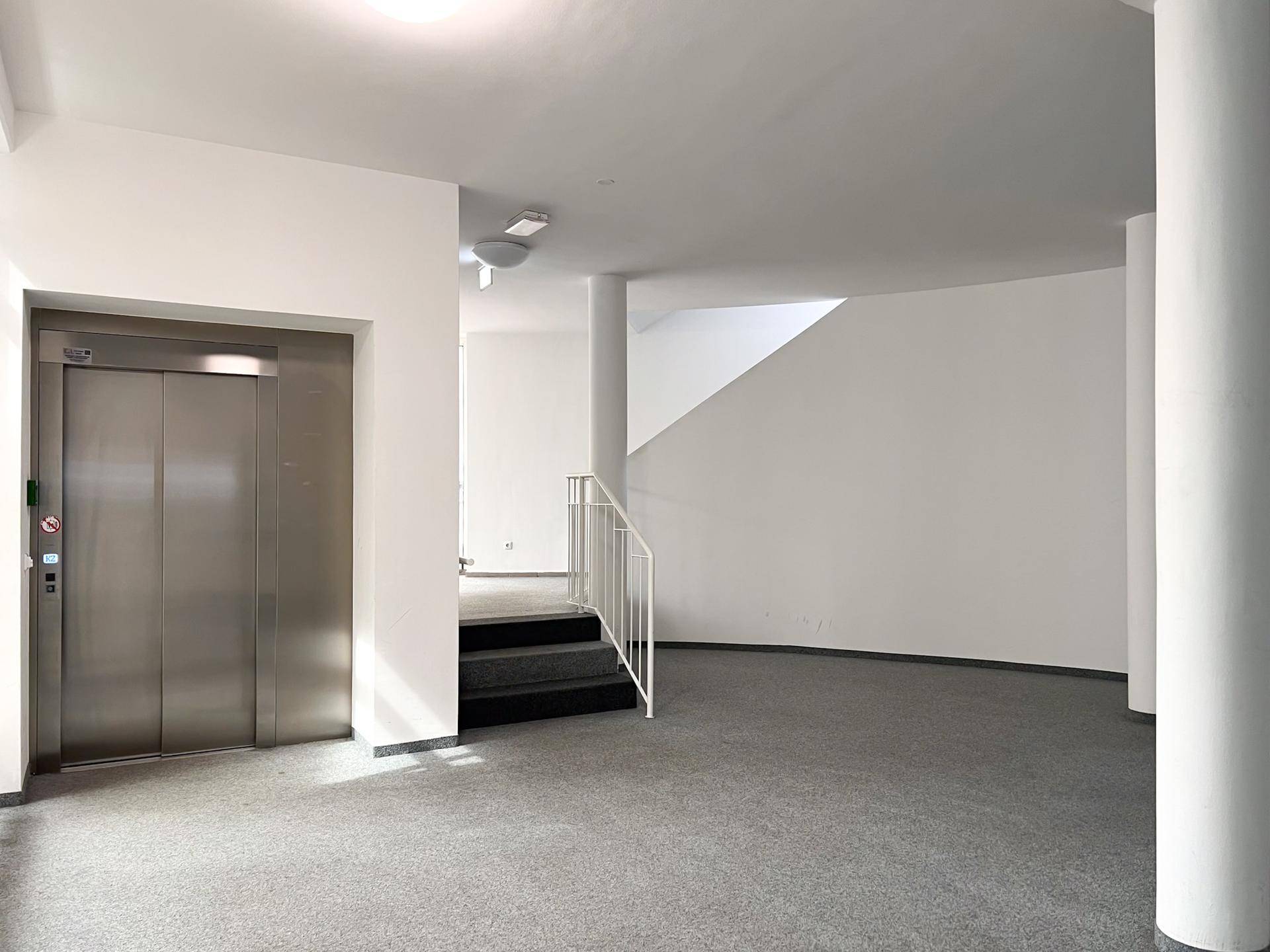 Heller Eingangsbereich mit modernem Aufzug und Treppenaufgang, ausgestattet mit Teppichboden.