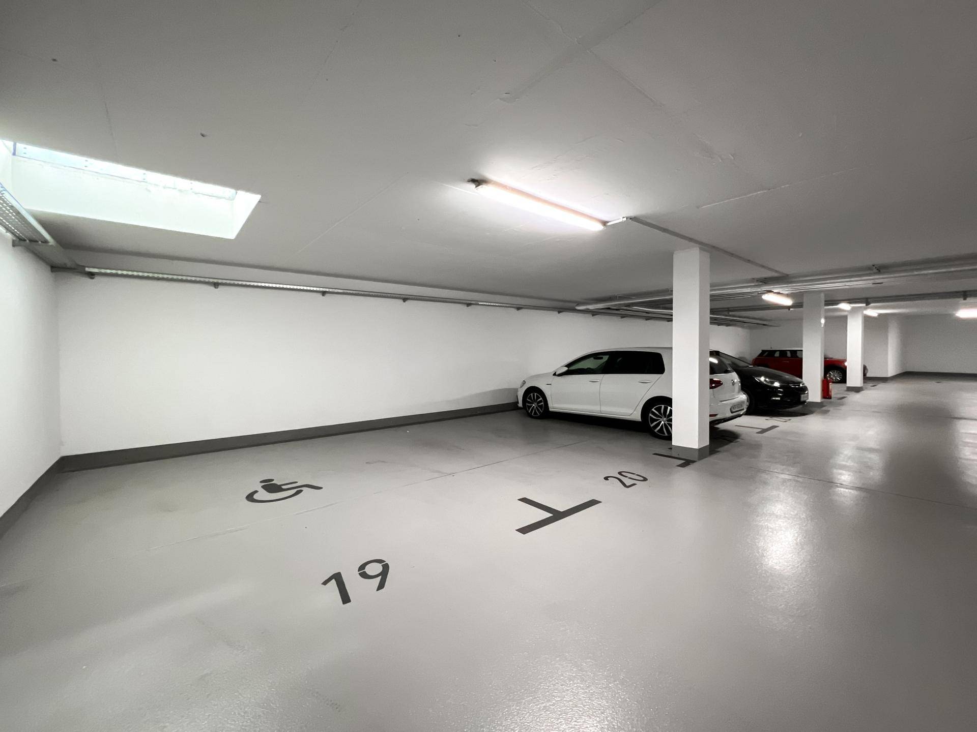 Saubere Tiefgarage mit markierten Stellplätzen, inklusive Behindertenparkplatz und Oberlicht.