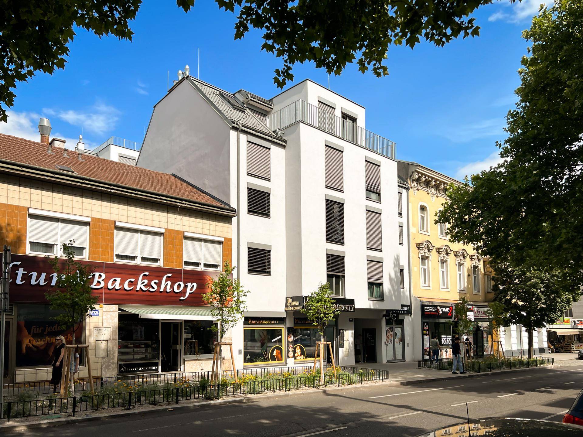 Stadtgebäude mit Geschäften im Erdgeschoss und modernen Wohnungen darüber an einer belebten Straße.
