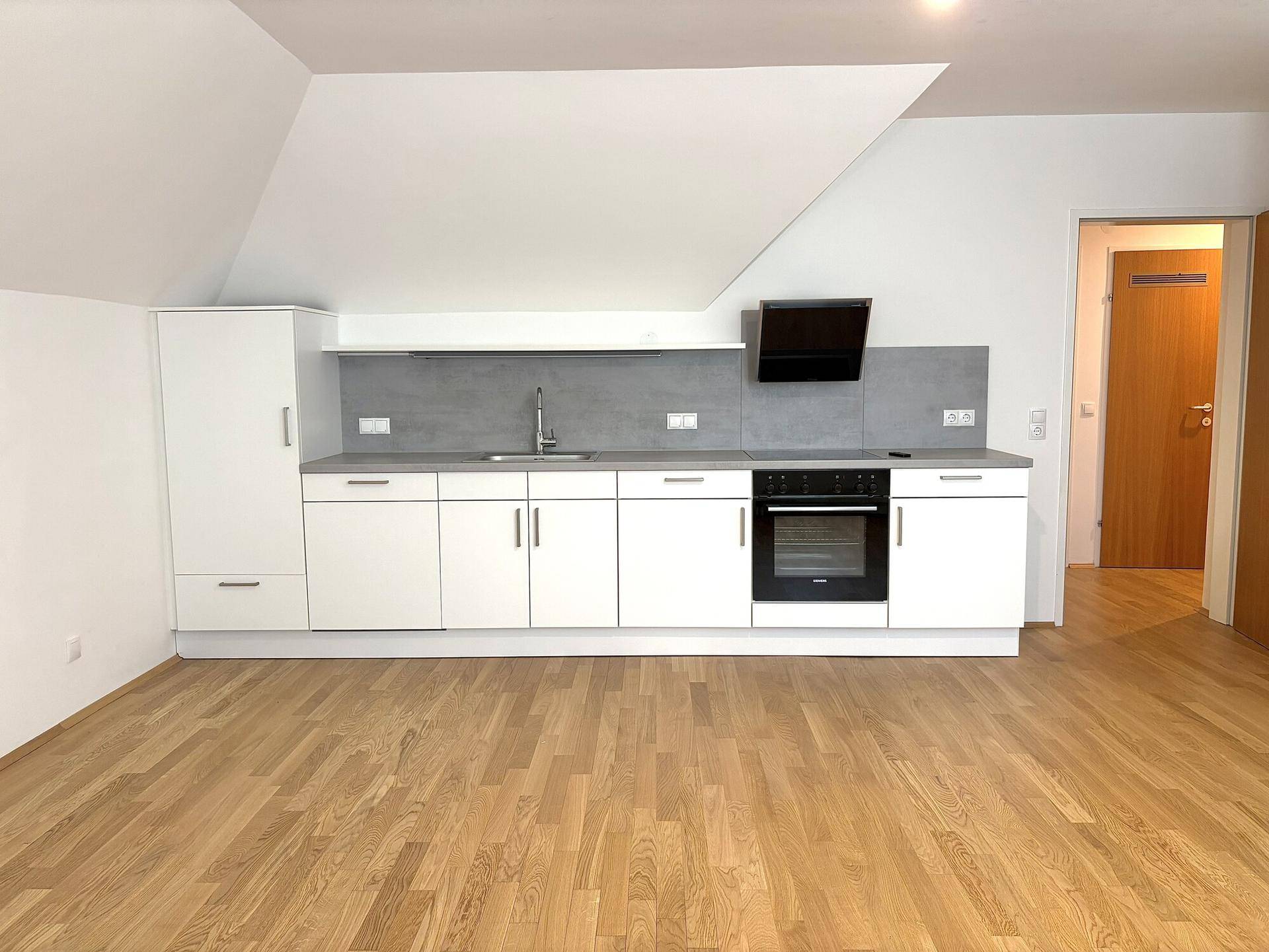 Detailansicht der modernen Einbauküche mit Backofen, Spüle und Dunstabzugshaube unter der Dachschräge.
