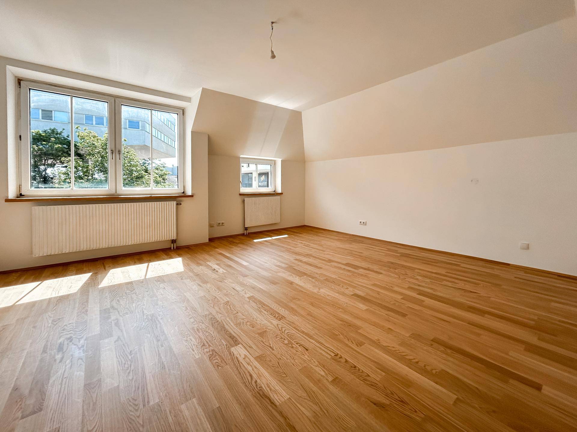 Geräumiger, heller Wohnbereich mit Holzboden, großen Fenstern und Blick ins Grüne.