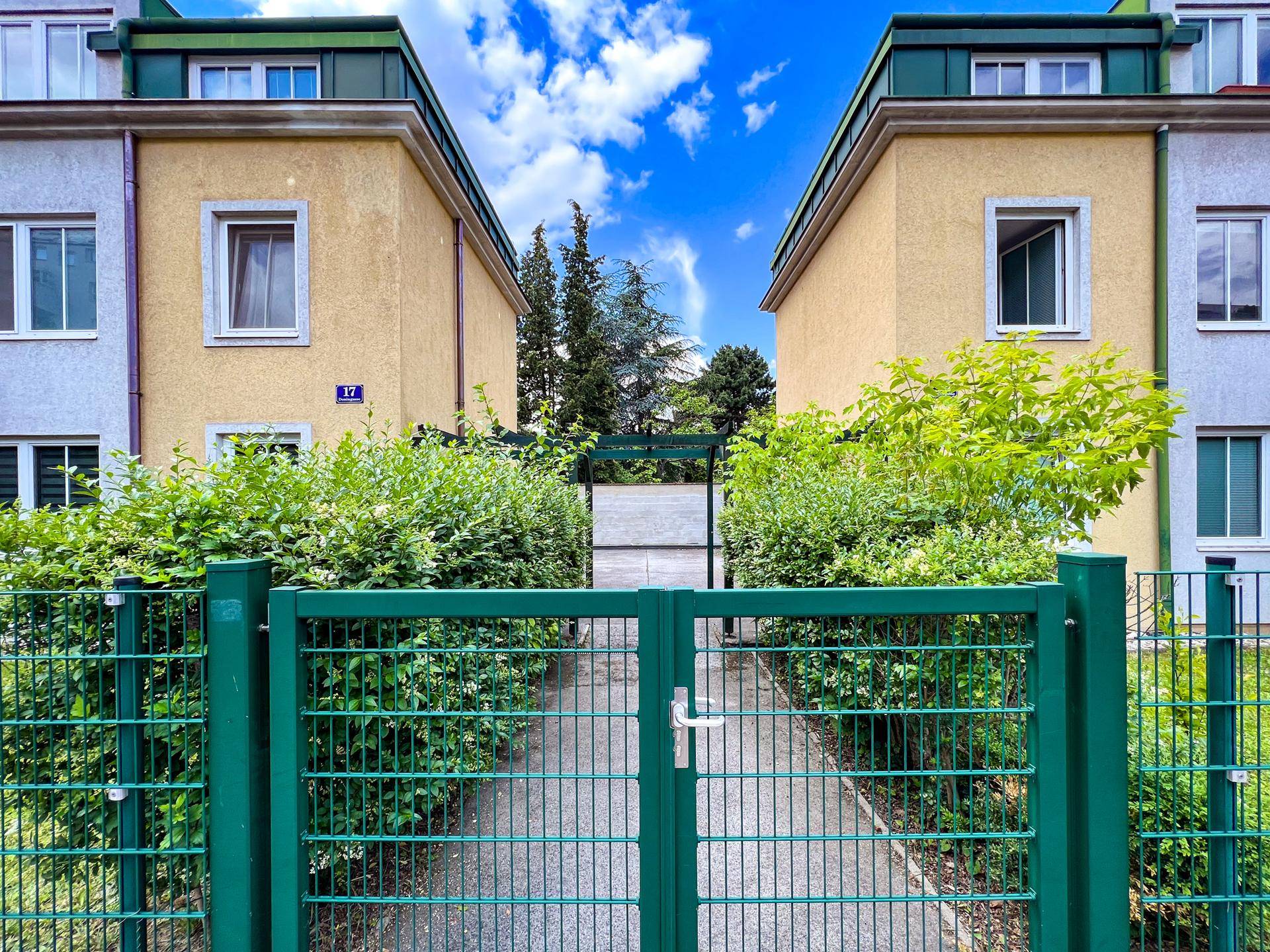Grünes Eingangstor zum Wohnkomplex, umgeben von gepflegten Hecken und Gebäudefassaden.