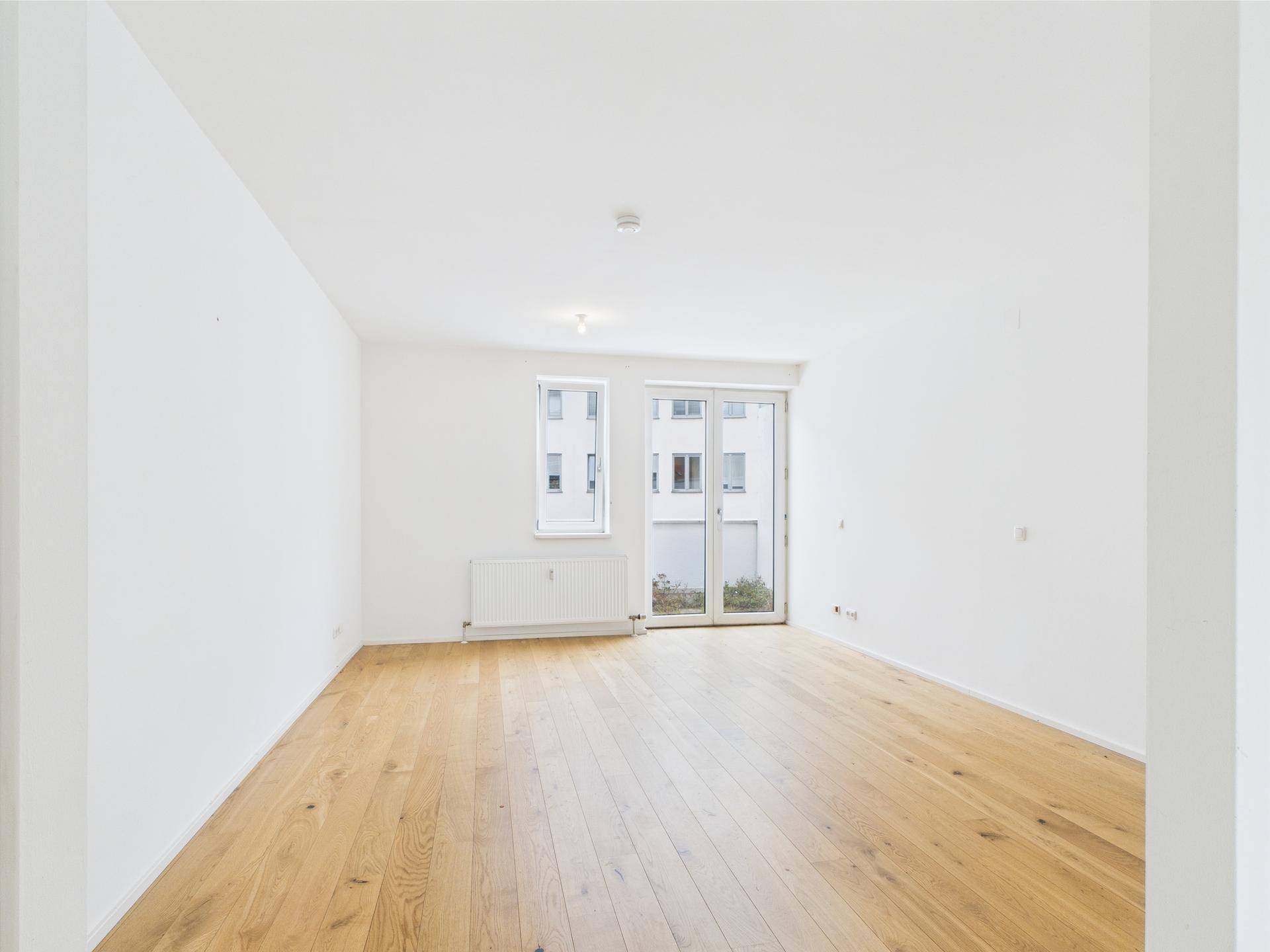 Heller Wohnraum mit Holzparkettboden und Zugang zu einem Außenbereich.