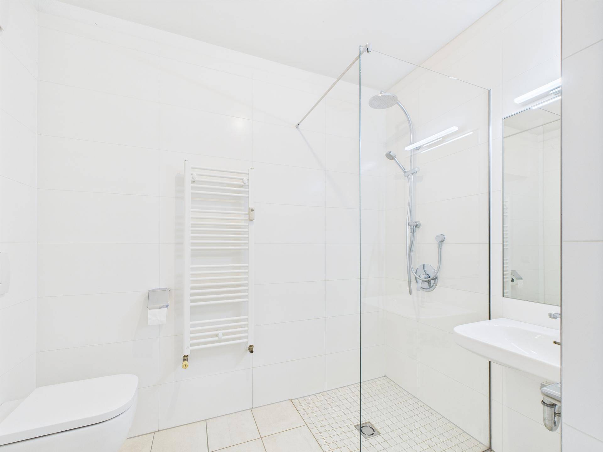Modernes Badezimmer mit weißen Fliesen, ebenerdiger Dusche und Handtuchheizkörper.