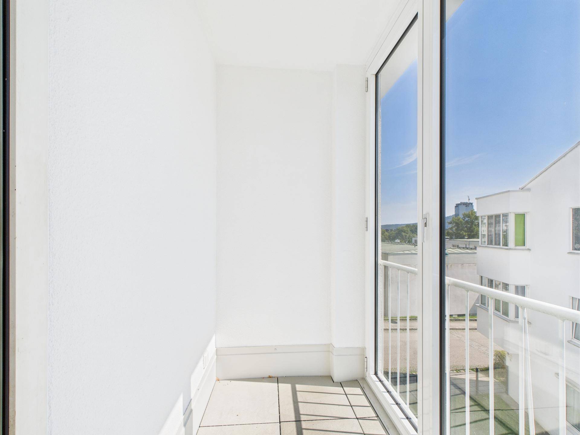 Schlichter Balkon mit weißer Fassade und Blick auf die benachbarten Gebäude.
