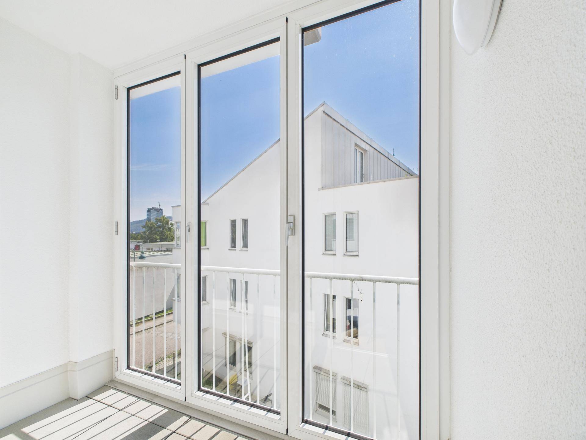 Sonniger Balkon mit weißem Geländer und Ausblick auf die moderne Wohnanlage.