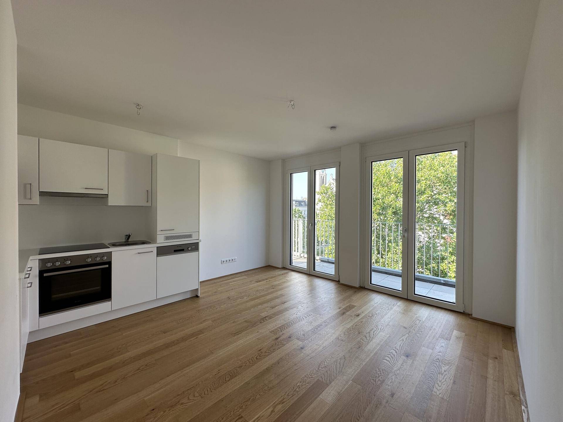 Heller Wohnbereich mit integrierter Küchenzeile, Holzboden und Zugang zum Balkon.