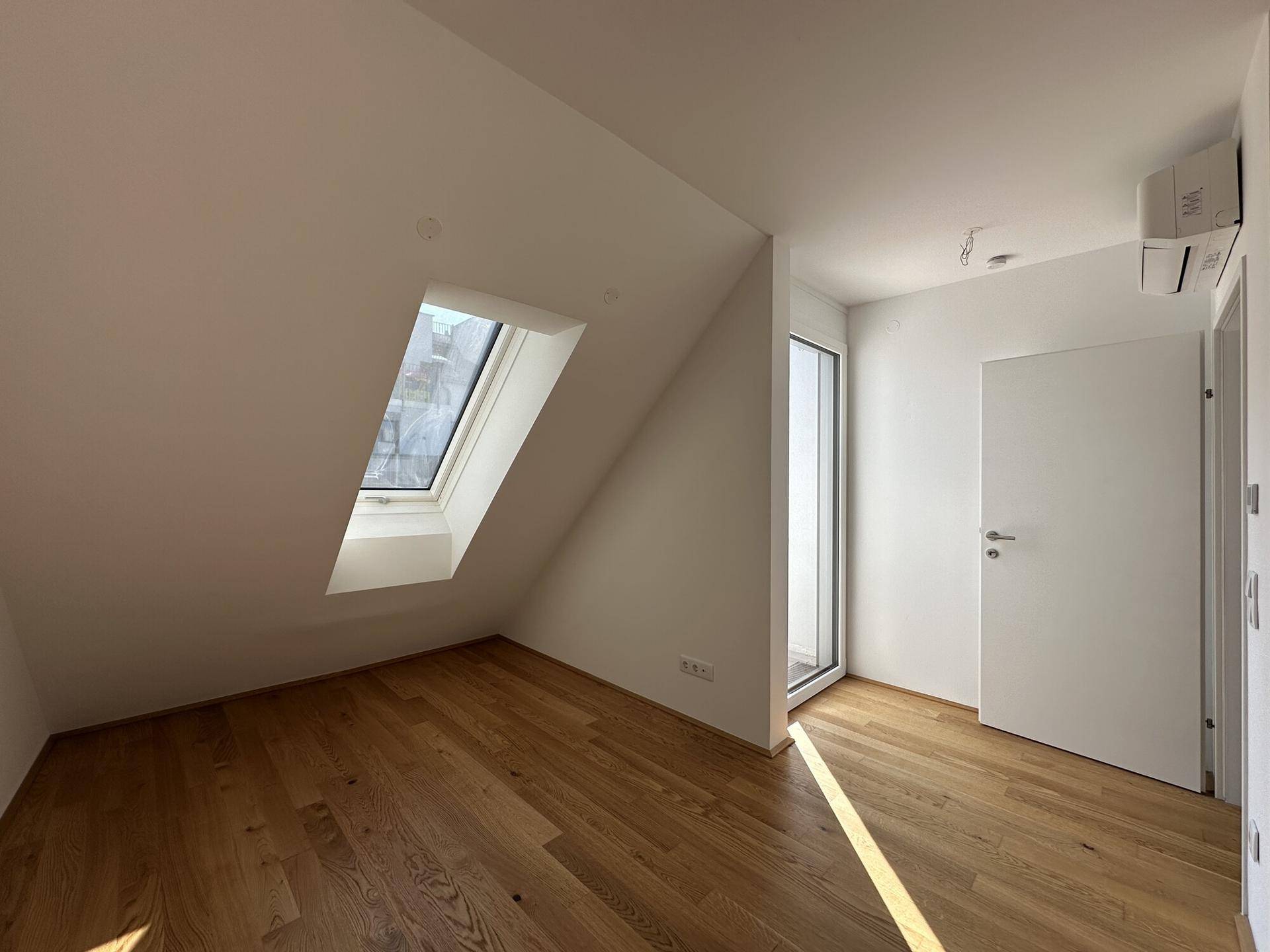Lichtdurchflutetes Zimmer mit Dachschräge, Holzboden und großem Dachfenster.