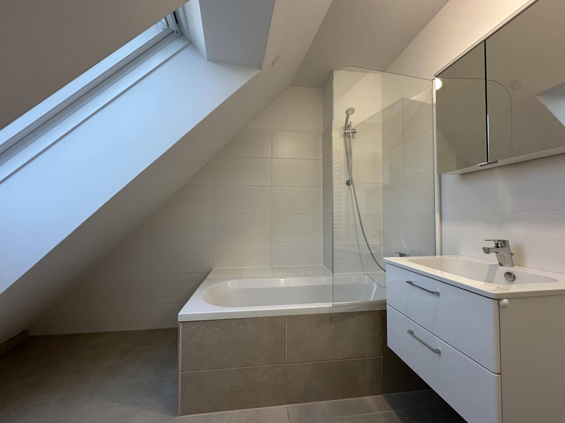 Modernes Badezimmer mit Badewanne, Dusche, Dachfenster und hellen Fliesen.