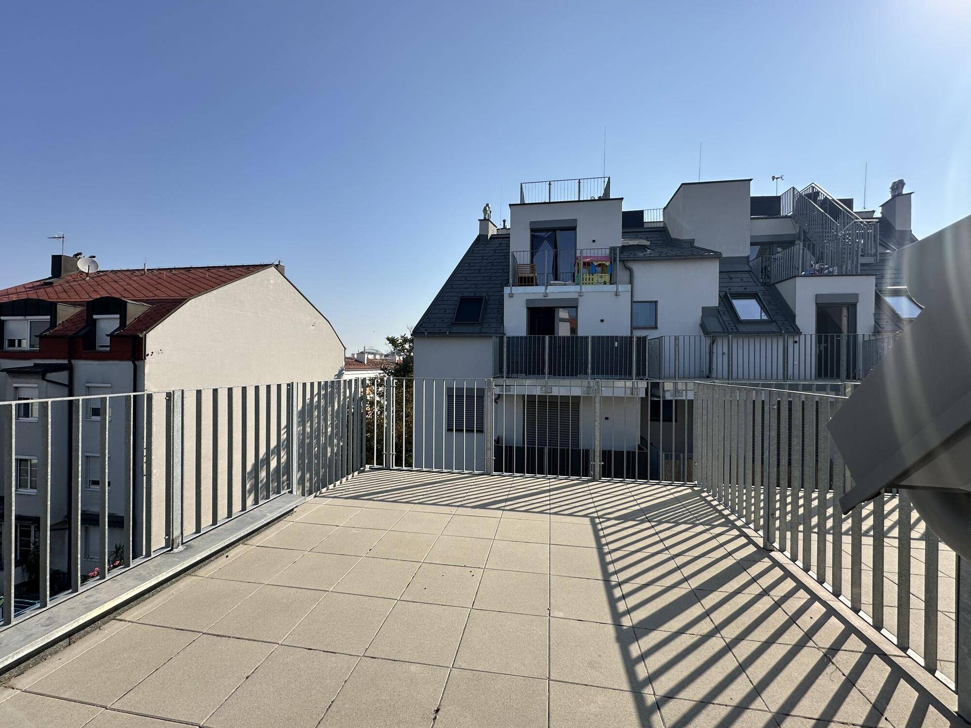 Geräumige Dachterrasse mit Fliesenboden und Blick auf die umliegenden Gebäude.