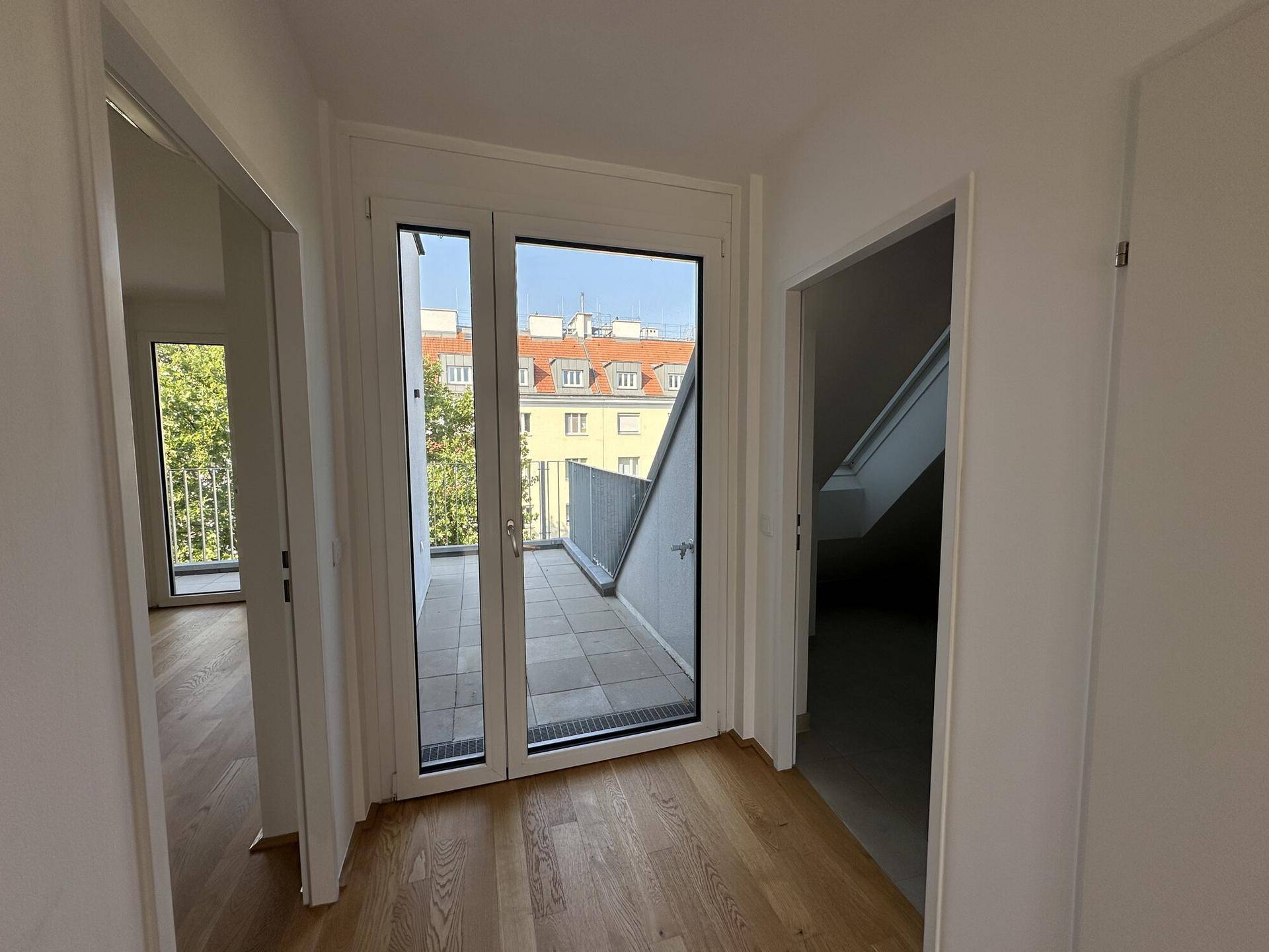 Heller Flur mit Holzboden und direktem Zugang zu einem gefliesten Balkon.