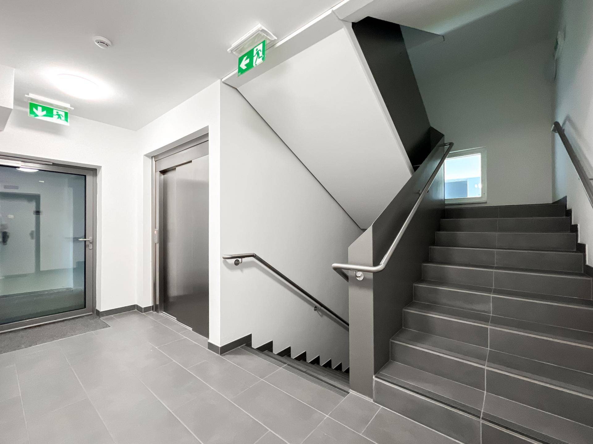 Heller Treppenaufgang mit Fliesenboden und modernem Aufzug im Gebäude.