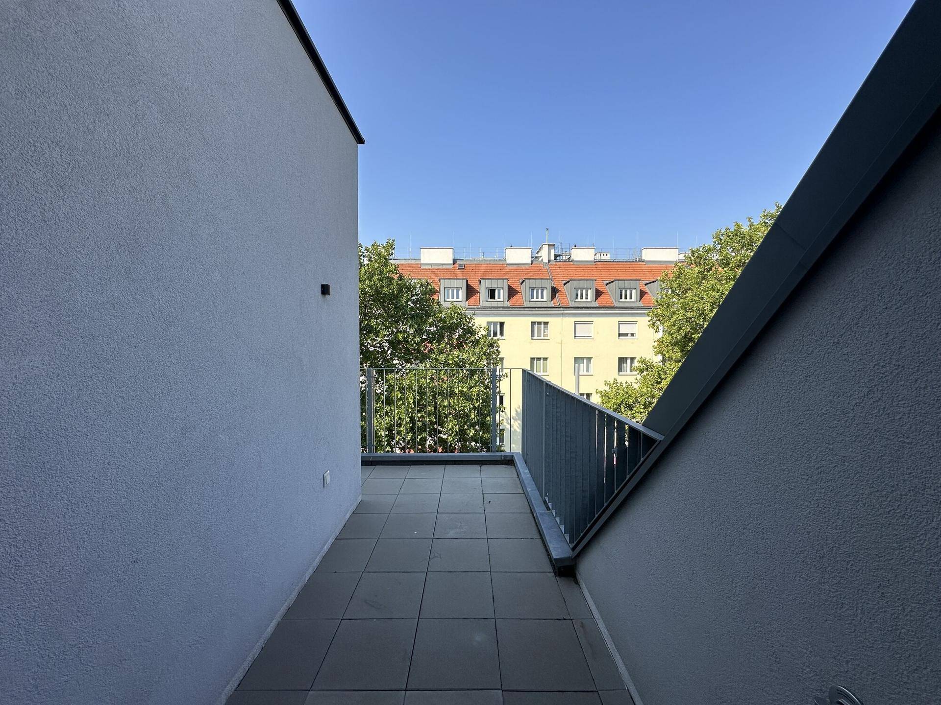 Langer, schmaler Balkon mit Fliesenboden und Blick auf die umliegenden Gebäude.
