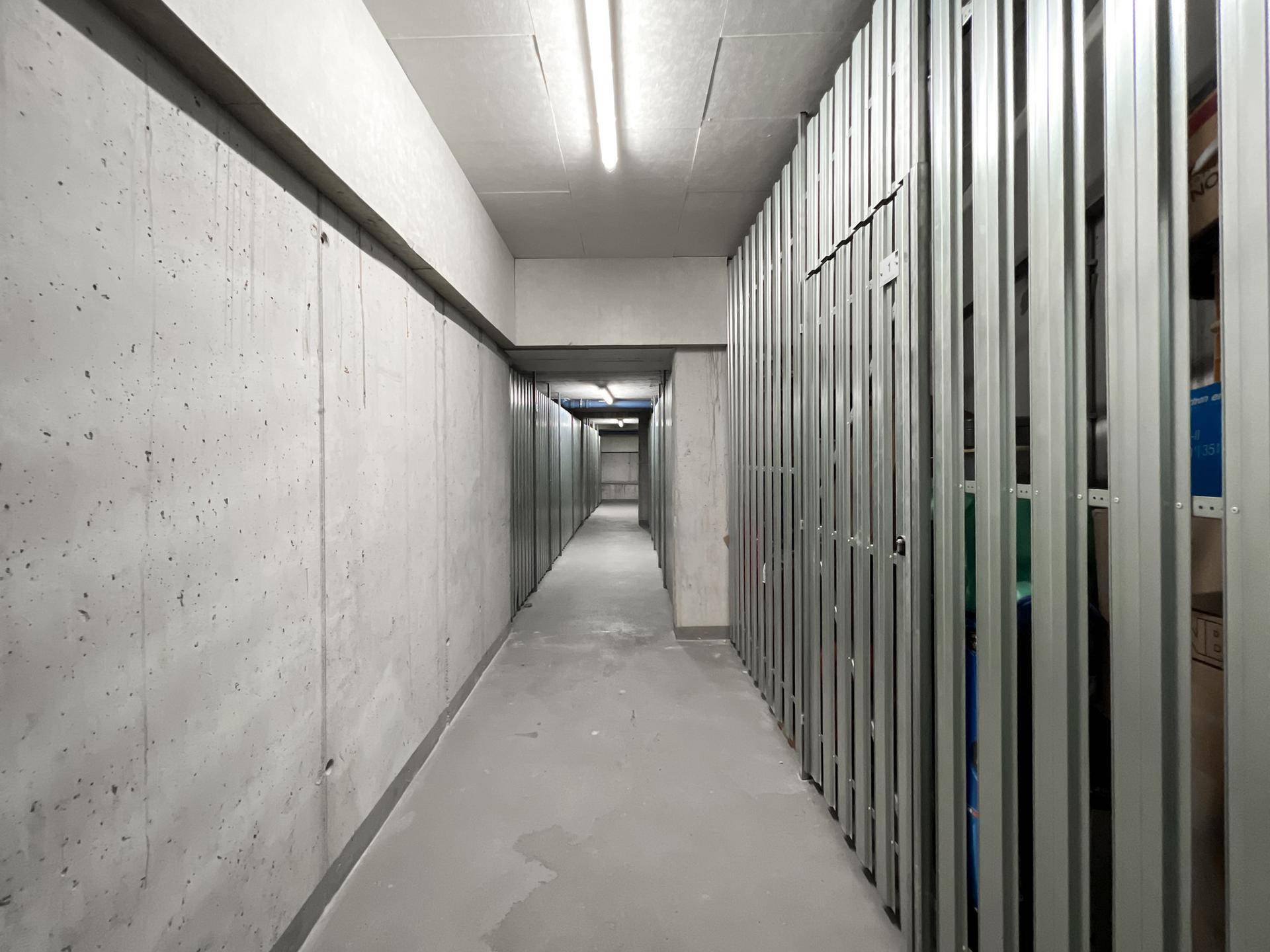 Langer Kellergang mit individuellen Abstellräumen und Betonwänden.