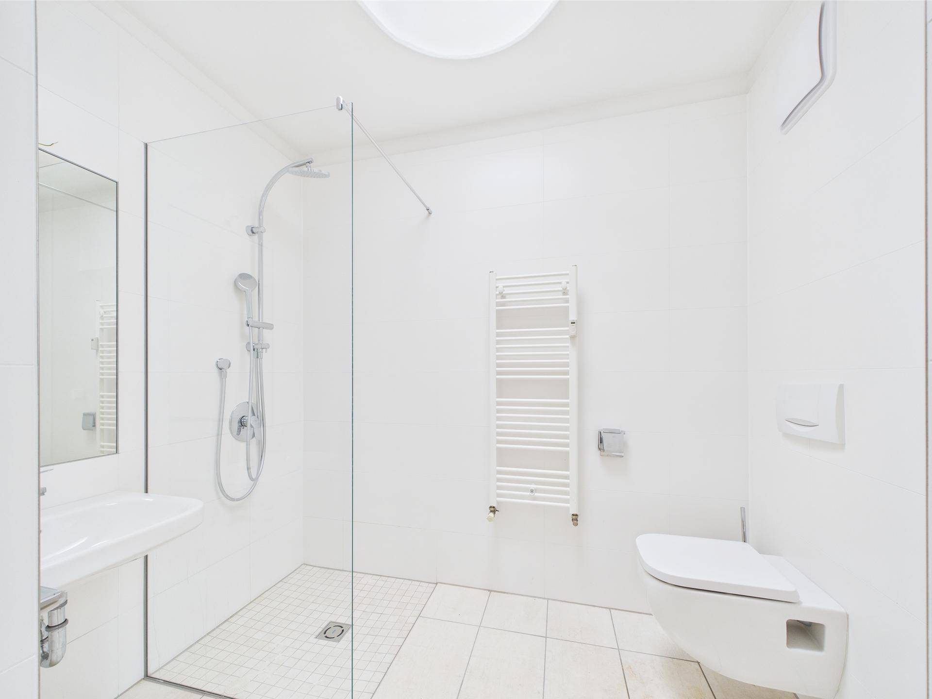 Modernes, hell gefliestes Badezimmer mit ebenerdiger Dusche, Wand-WC und Handtuchheizkörper.