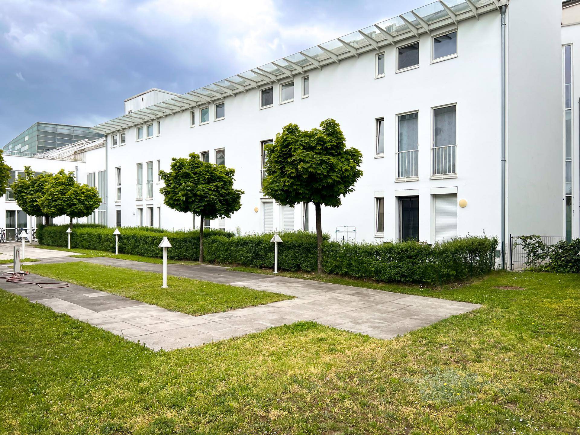 Heller Innenhof mit gepflegten Grünflächen, Hecken und Bäumen vor modernen Gebäuden.