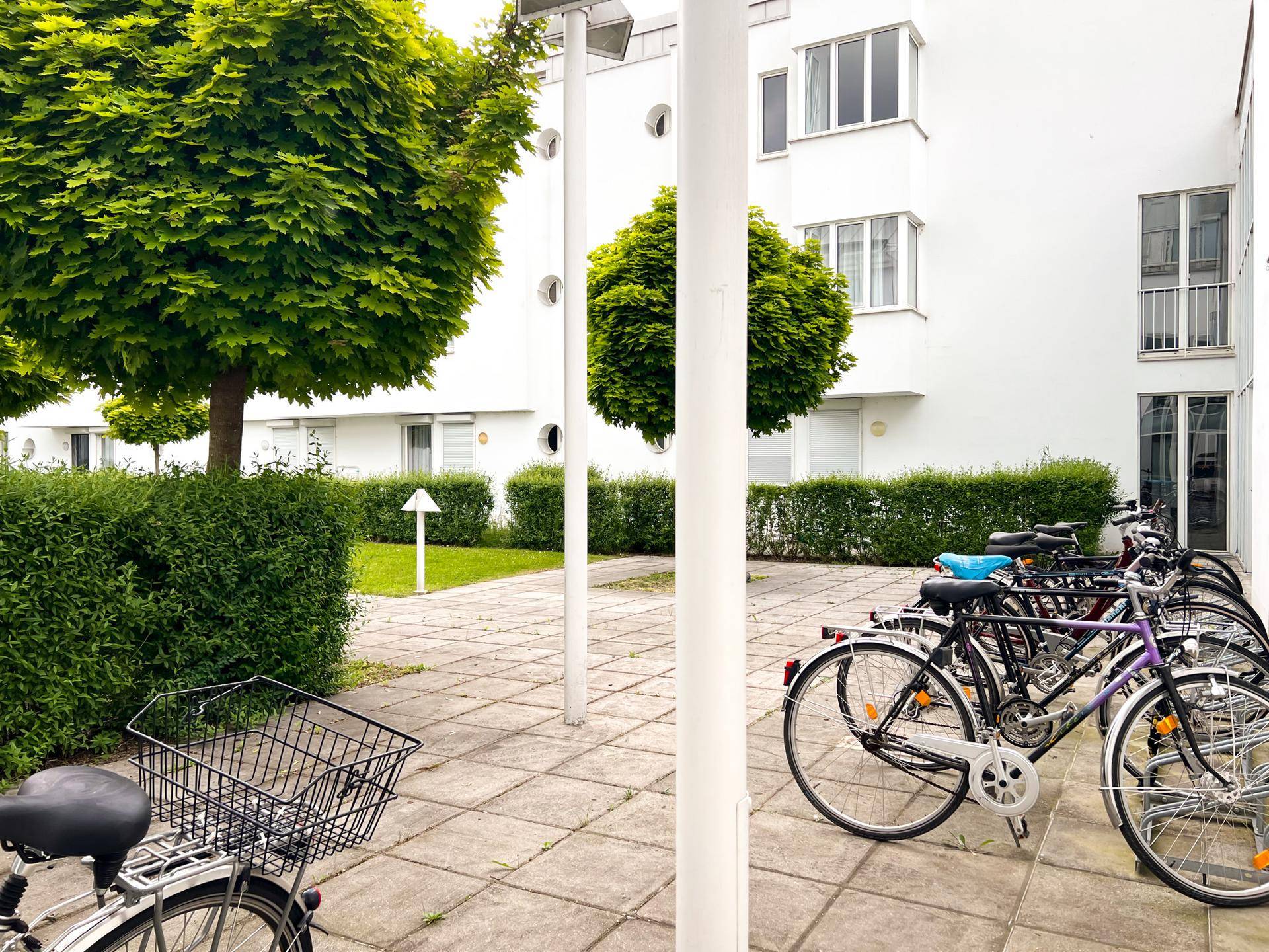 Fahrradabstellplatz im begrünten Innenhof der Wohnanlage mit Bäumen und Hecken.