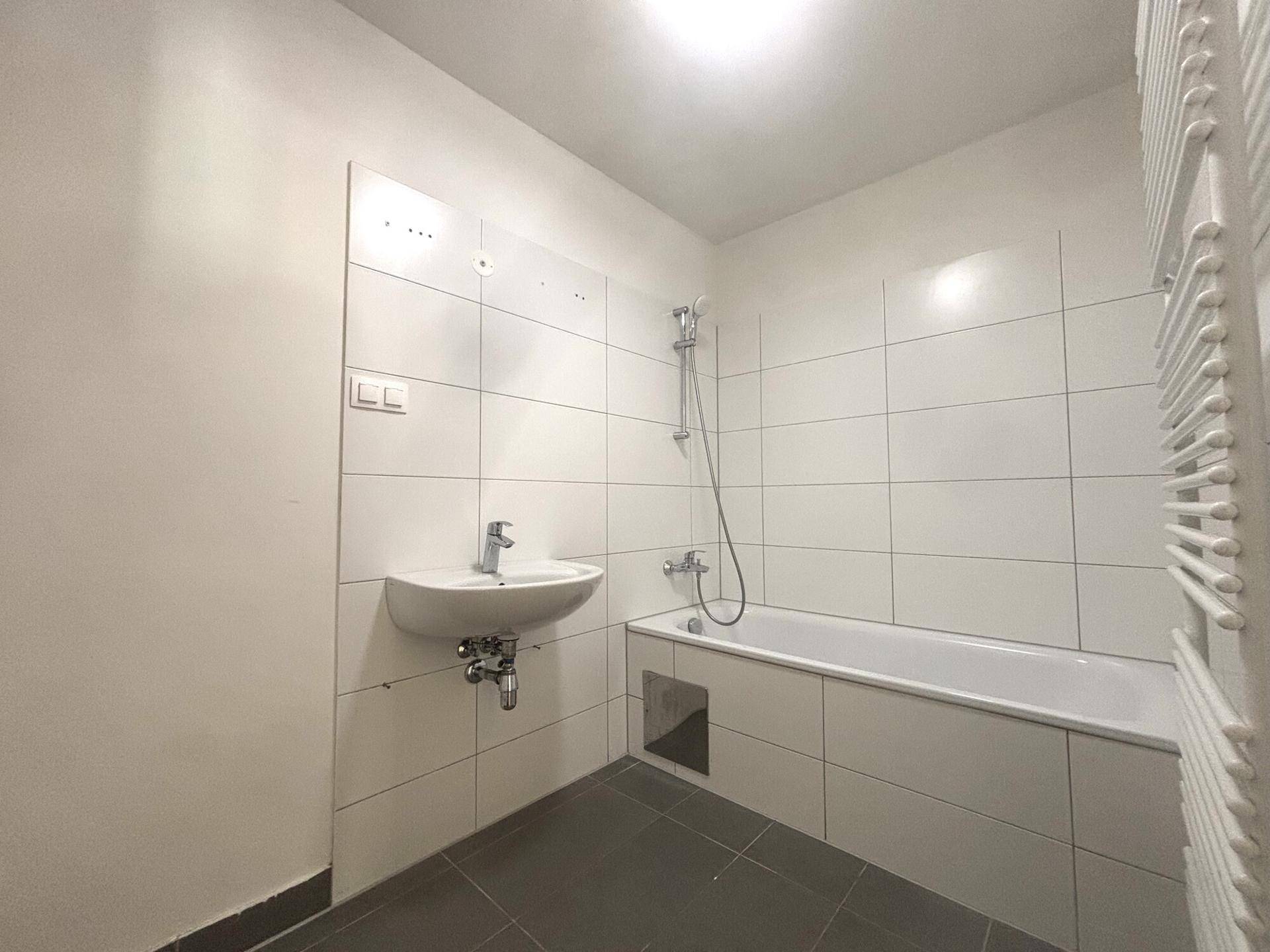 Modernes Badezimmer mit Badewanne, Einzelwaschbecken, weißen Wandfliesen und beheiztem Handtuchhalter.