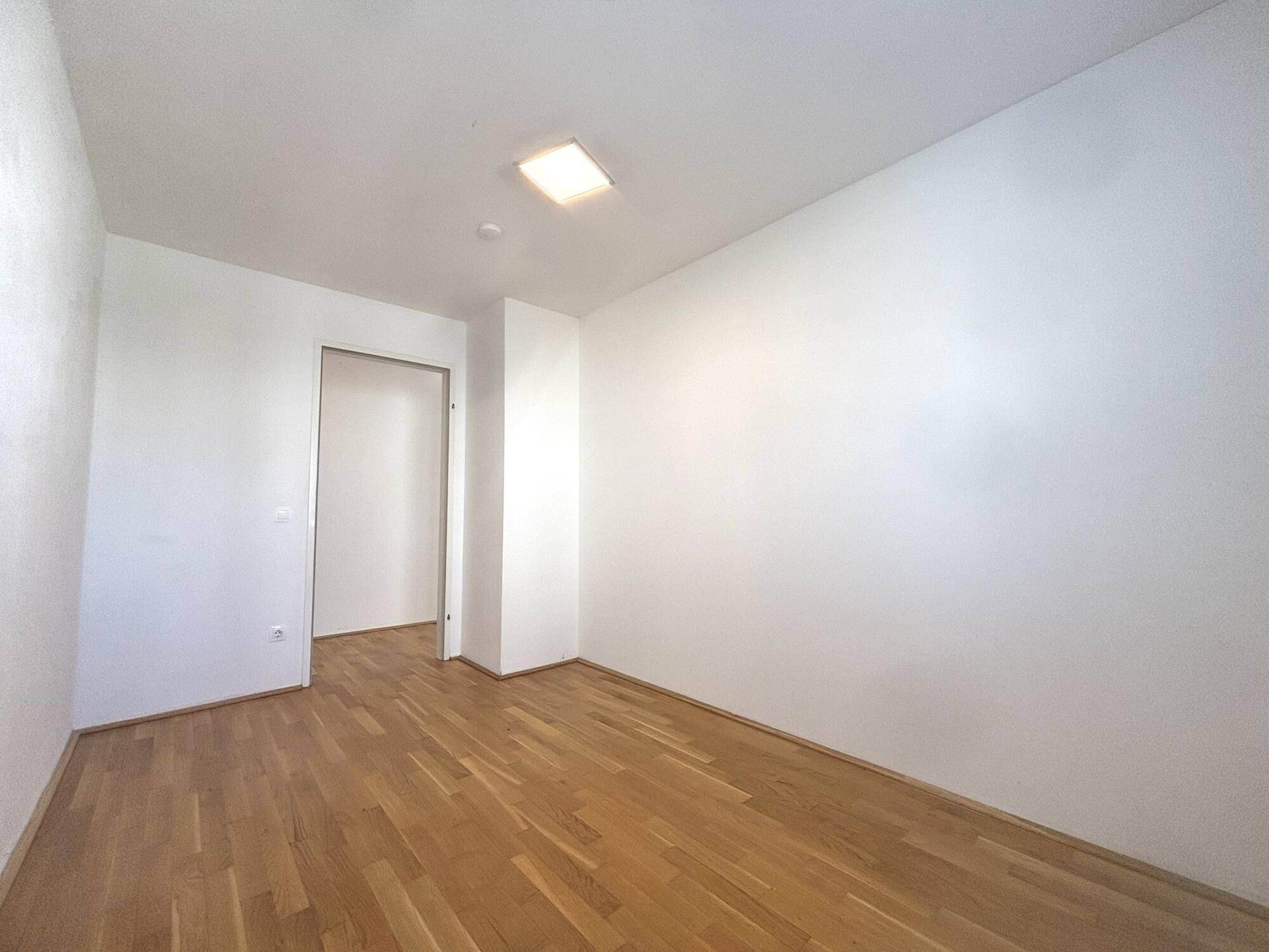 Helles, leeres Zimmer mit Parkettboden und weiß gestrichenen Wänden, bereit zur individuellen Gestaltung.