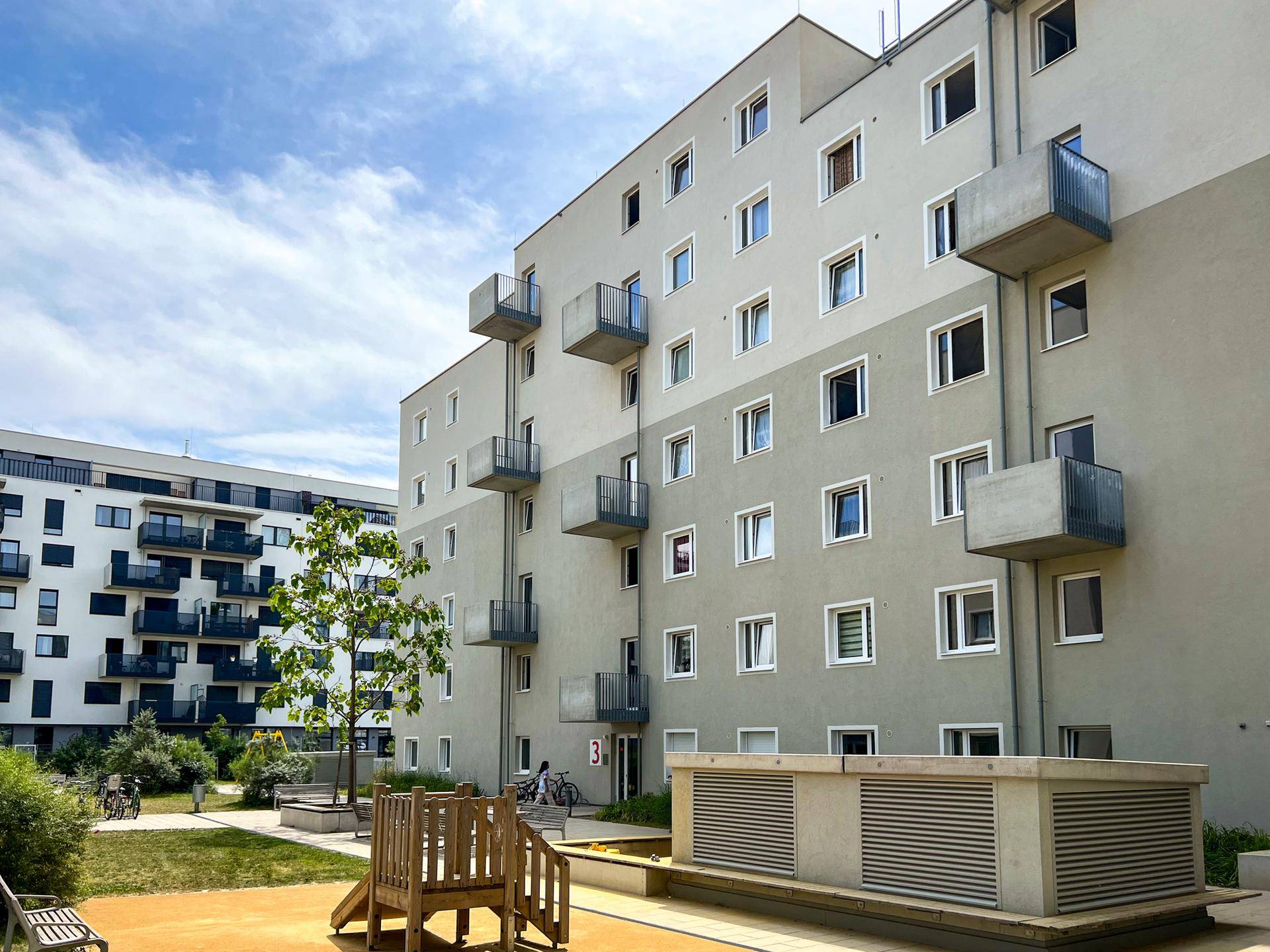 Moderne Wohnfassade mit Balkonen und einem kleinen Spielplatzbereich im begrünten Innenhof.