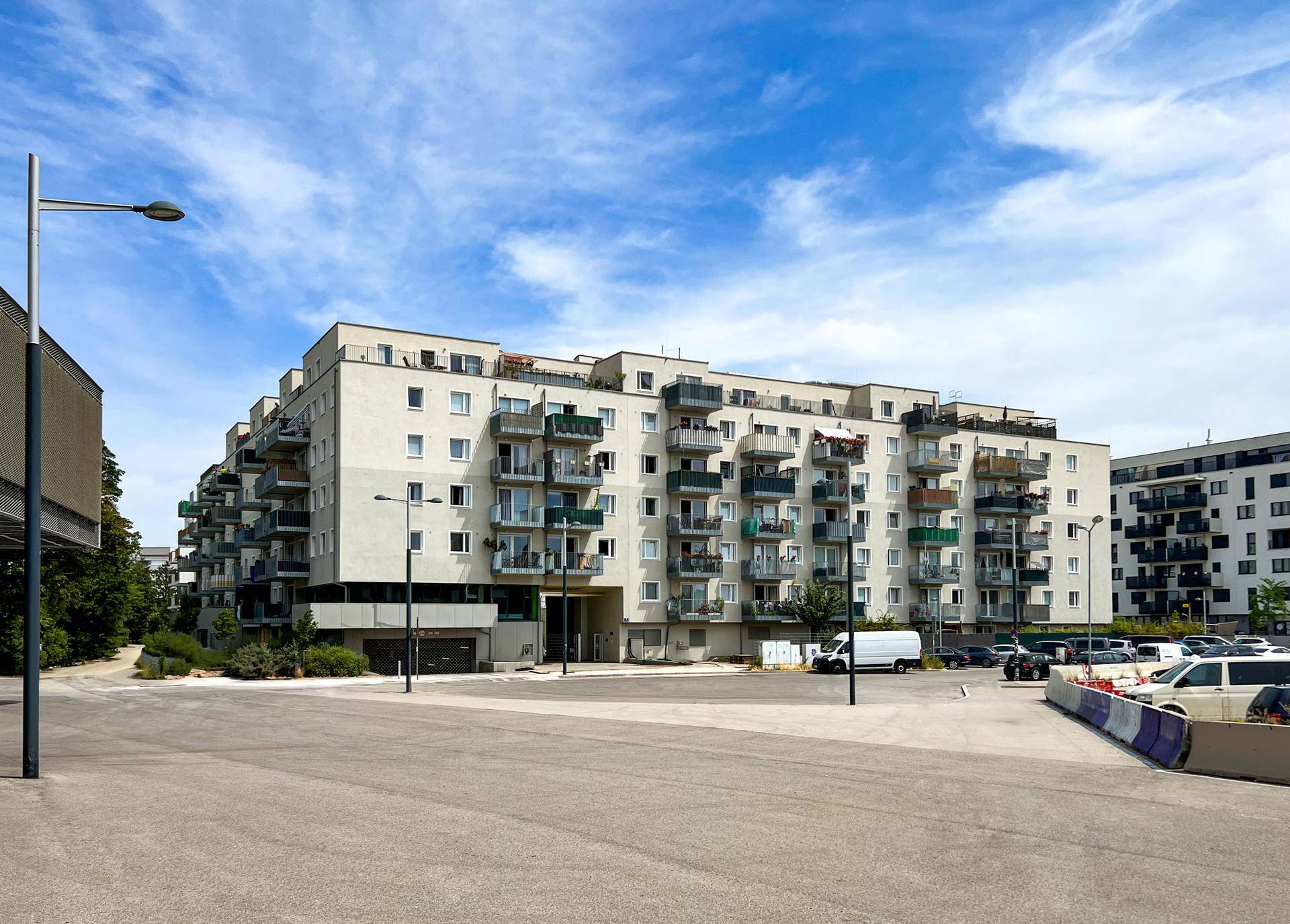 Moderne Wohnanlage mit zahlreichen Balkonen und einem großen Parkplatz im Vordergrund.