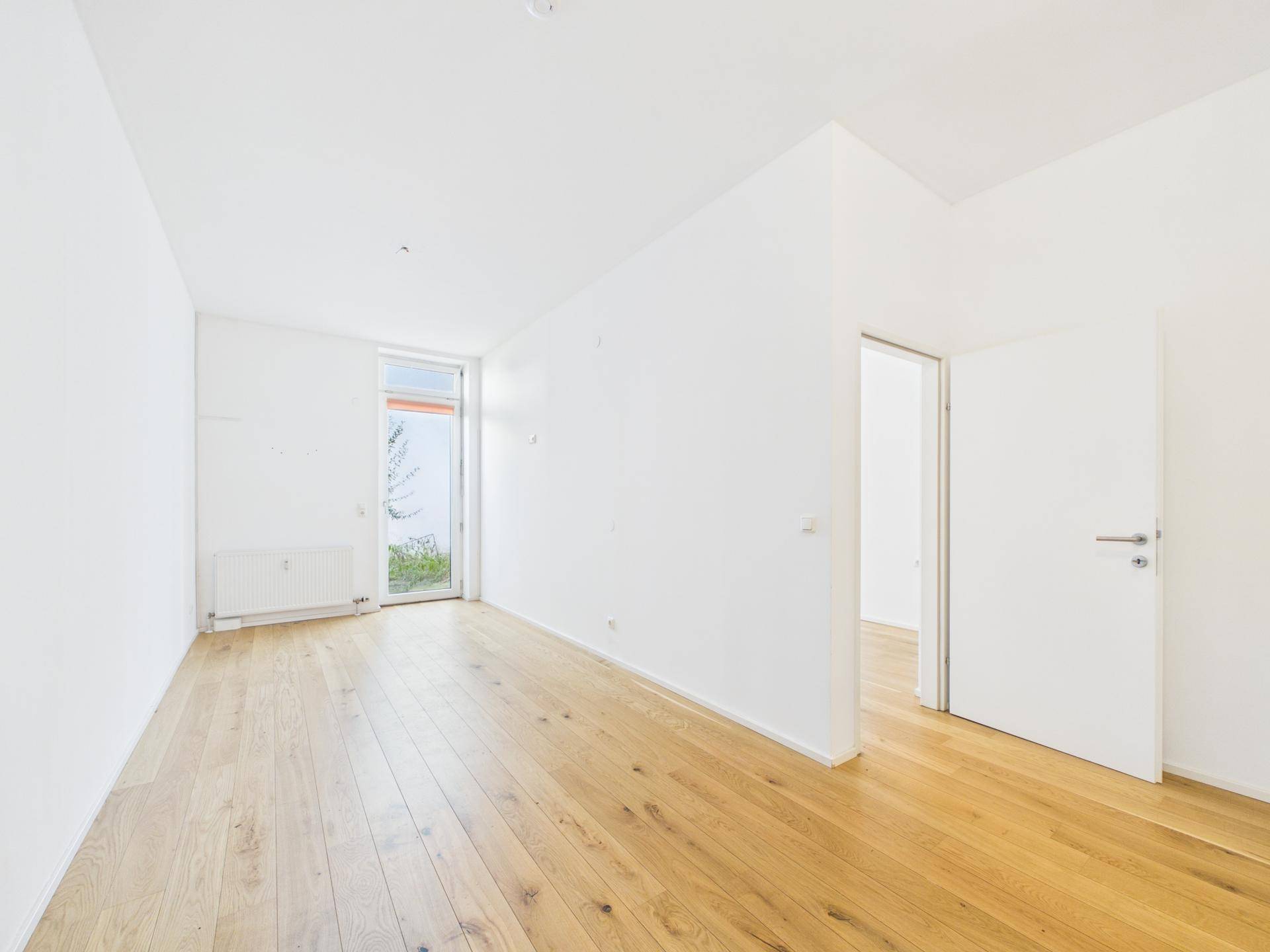 Geräumiger, heller Raum mit Holzboden und großem Fenster, das viel Tageslicht hereinlässt.