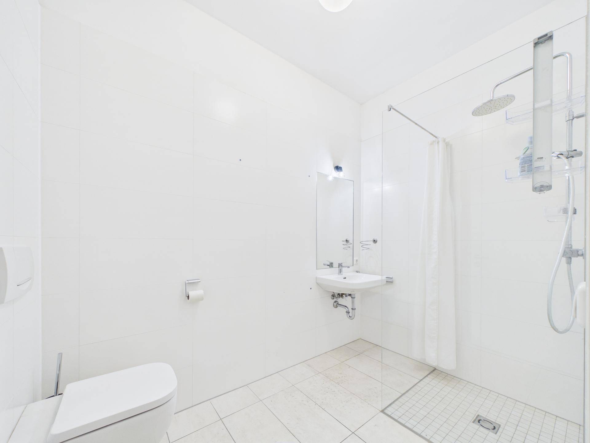 Modernes Badezimmer mit weißen Fliesen, ebenerdiger Dusche und Wand-WC.