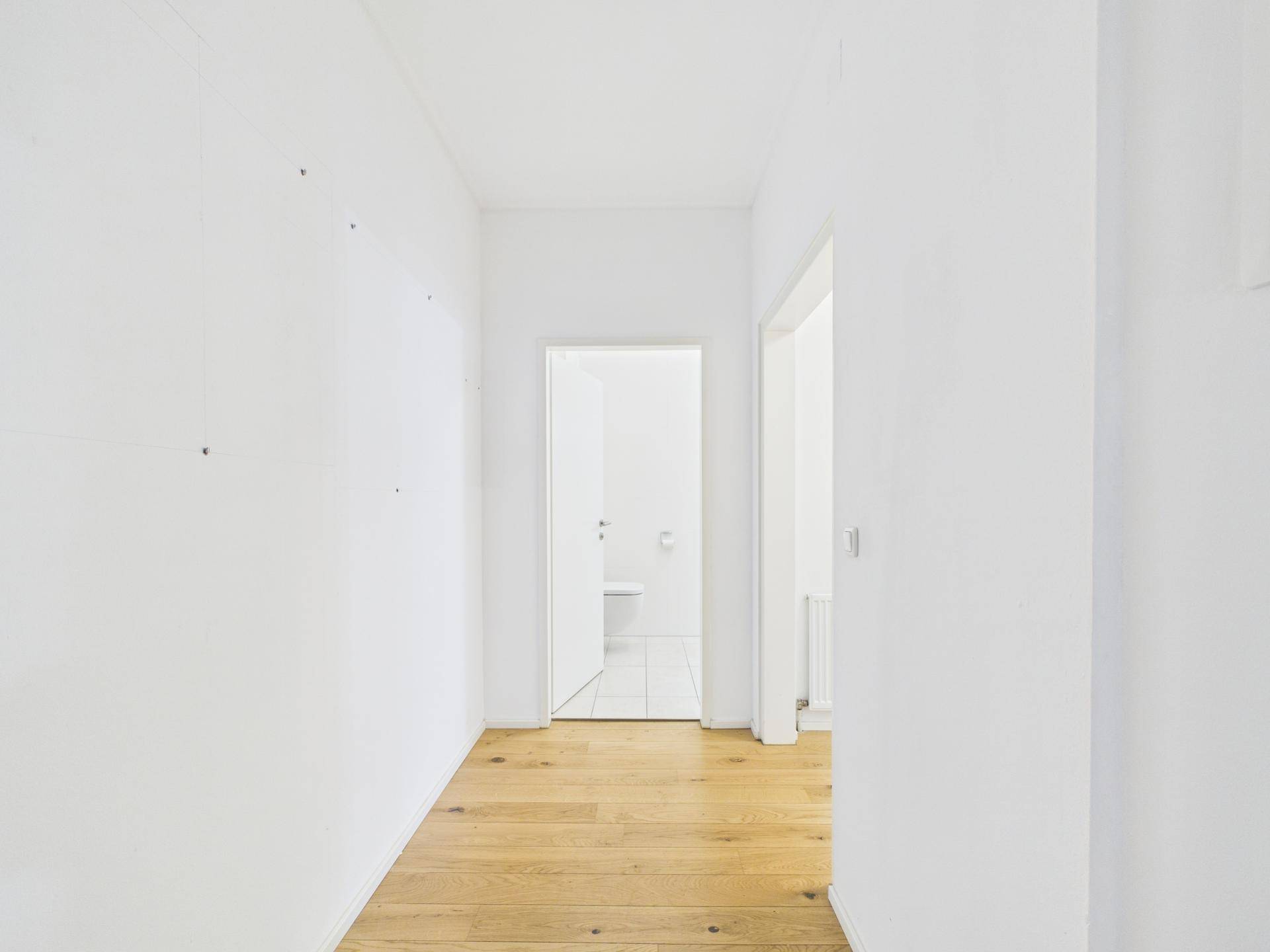 Heller Flur mit Holzboden und Zugang zu weiteren Zimmern, inklusive Badezimmer.