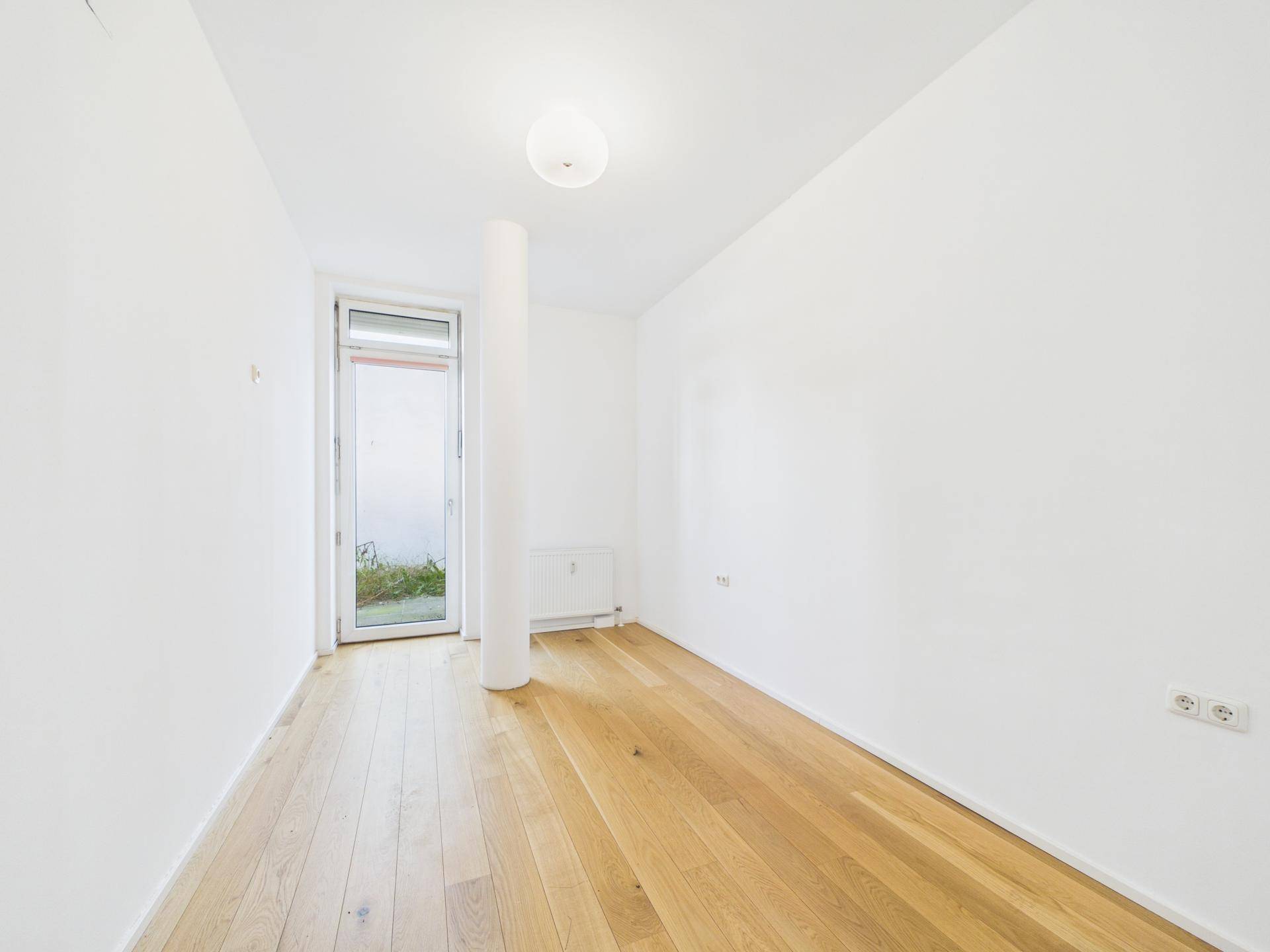 Kleiner, heller Raum mit Holzboden und Zugang zu einem Außenbereich, ideal als Schlafzimmer.