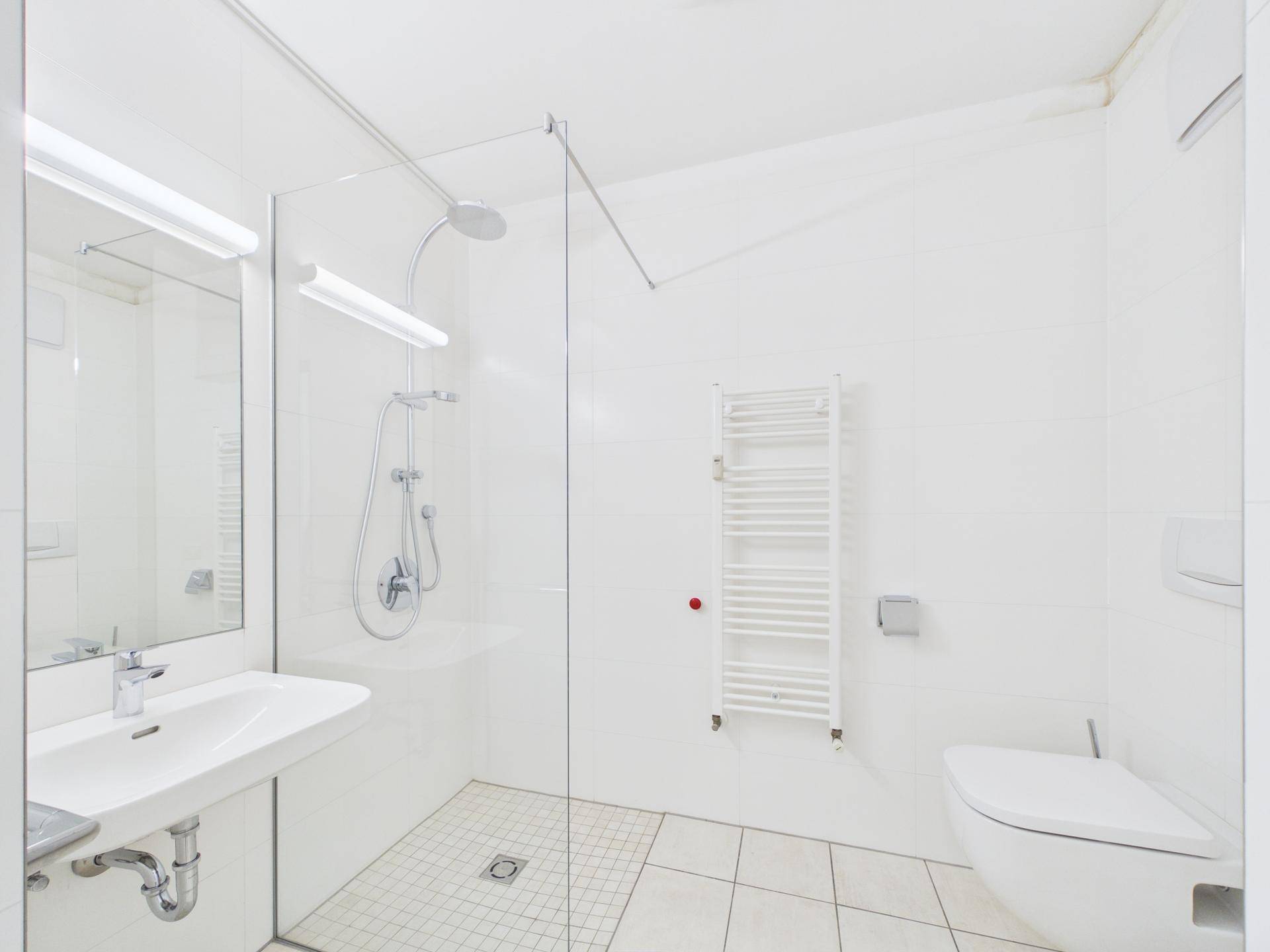 Modernes Badezimmer mit ebenerdiger Dusche, Wand-WC und beheiztem Handtuchhalter in Weiß gehalten.