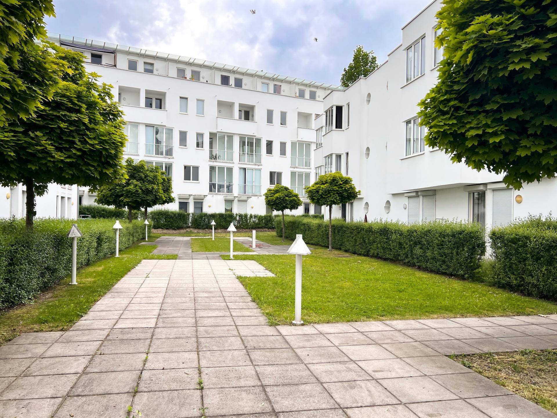 Gemeinschaftsgarten mit Rasenflächen, Bäumen und gepflasterten Wegen zwischen den modernen Gebäuden.