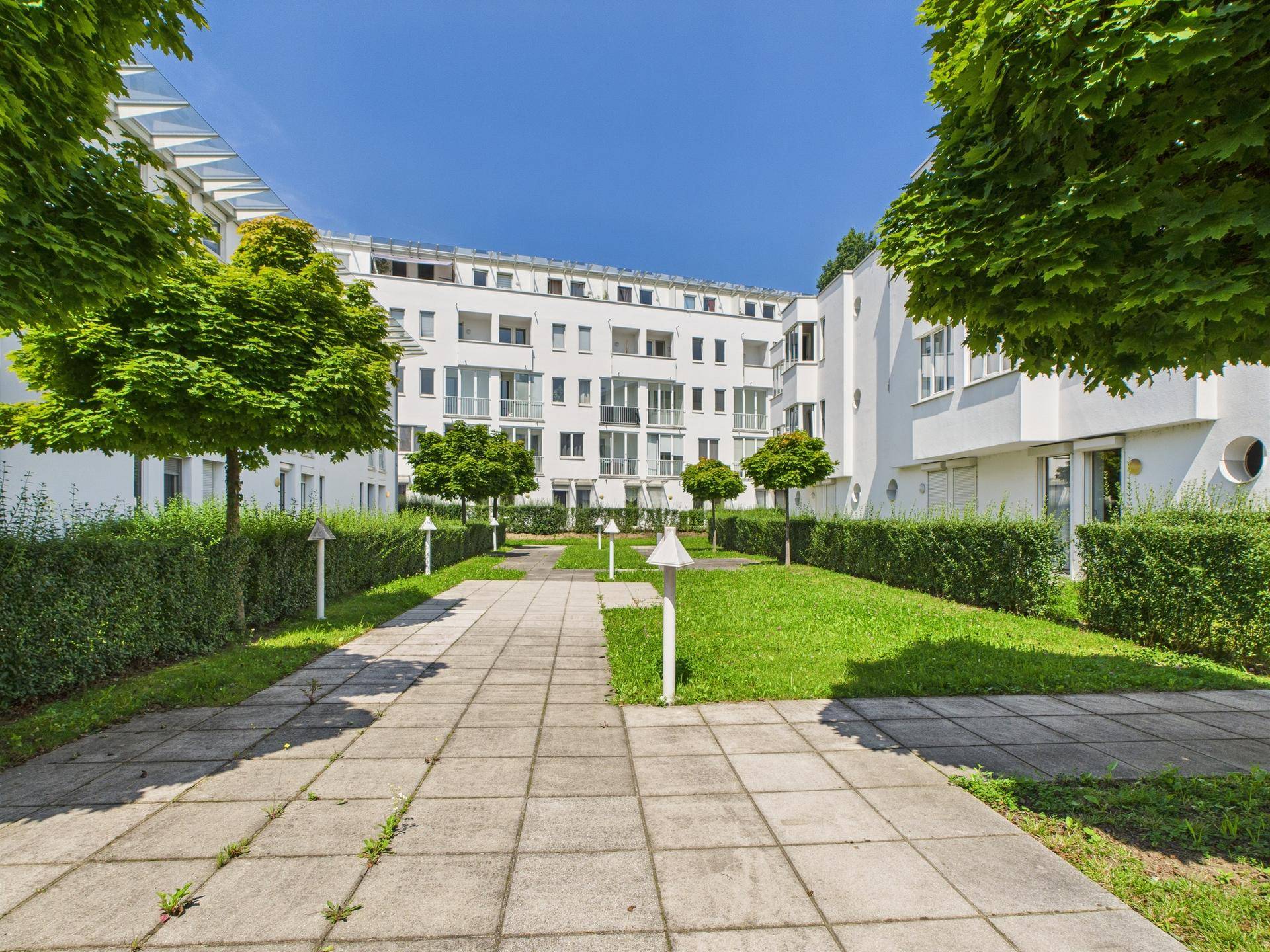 Weitläufiger Innenhof mit Rasenflächen, Bäumen und Wegen, umgeben von modernen Wohngebäuden.