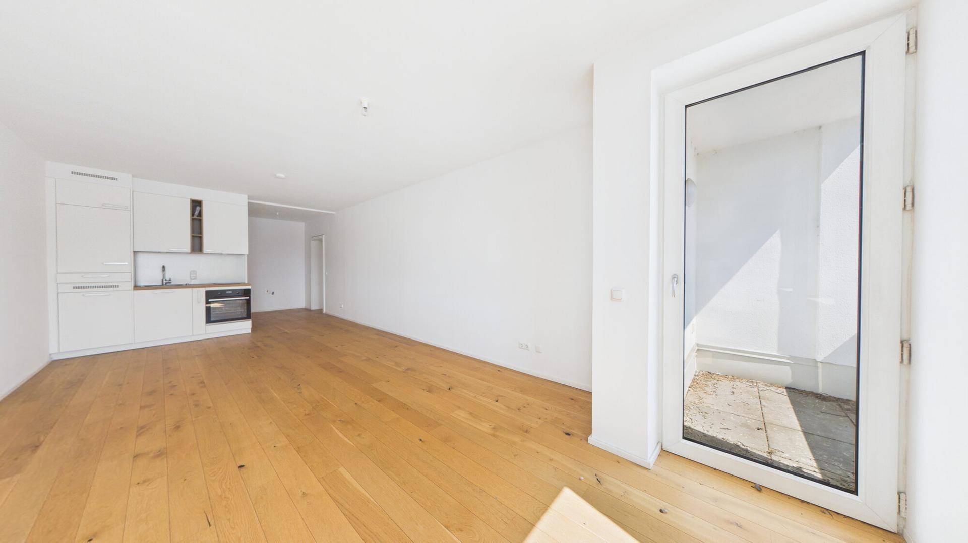 Geräumiger Wohnbereich mit Holzboden und Zugang zu einem Balkon oder einer Terrasse.