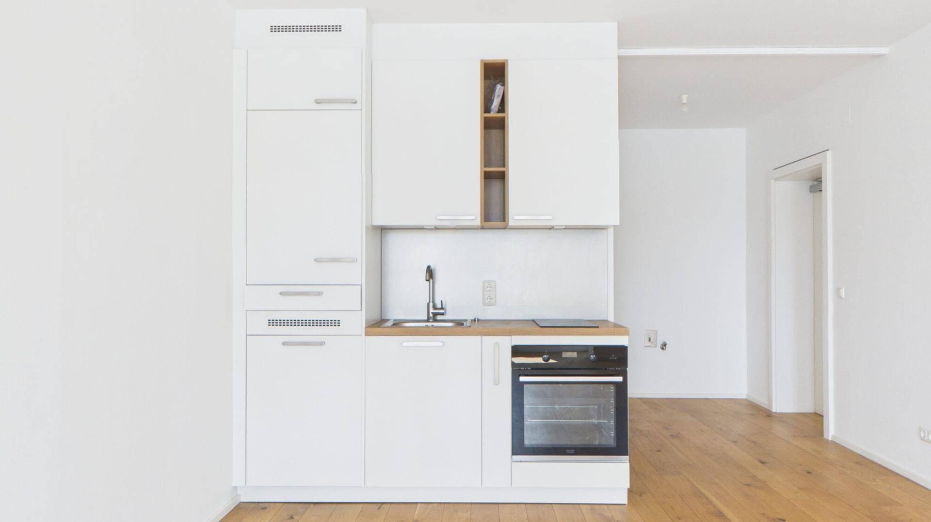 Moderne, weiße Küchenzeile mit integriertem Backofen und Holzarbeitsplatte in einem hellen Raum.