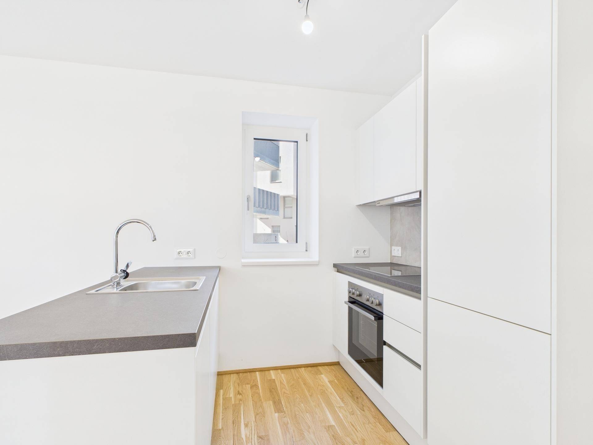 Moderne Einbauküche mit weißer Front, dunkler Arbeitsplatte, integriertem Backofen und Spülbecken.