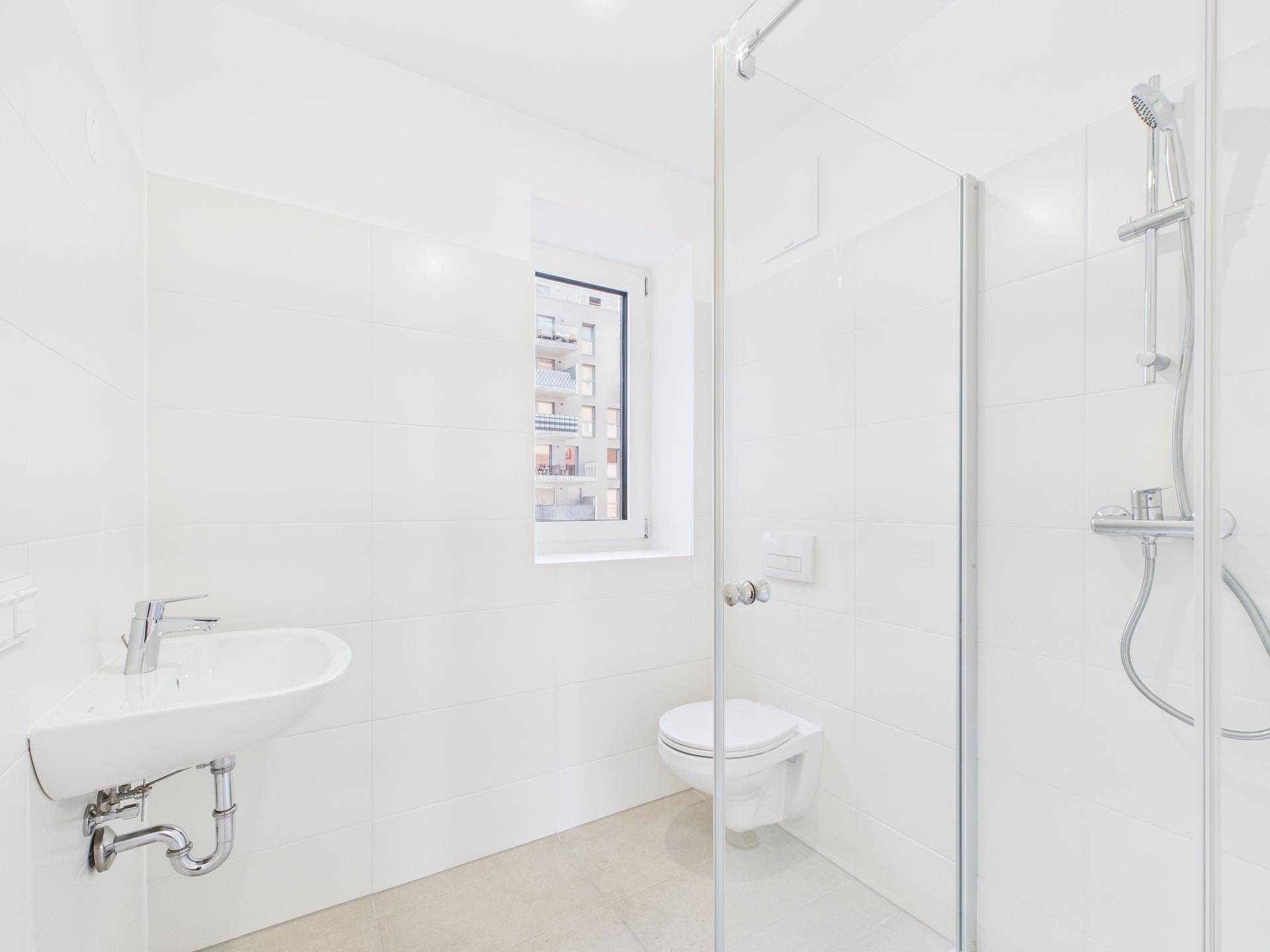 Helles Badezimmer mit Dusche, WC, Waschbecken und Fenster, komplett in weißen Fliesen gehalten.