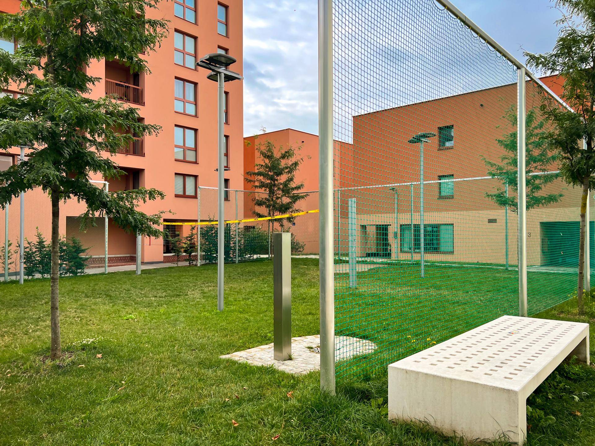 Gemeinschaftlicher Gartenbereich mit Rasenfläche, Sitzbank und Sportnetz zwischen modernen Wohngebäuden.
