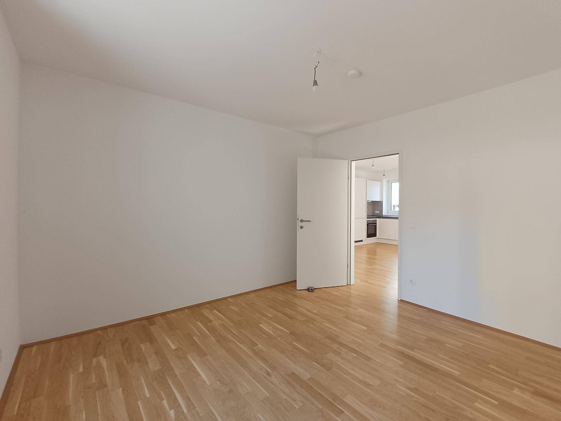 Geräumiges Zimmer mit Parkettboden und Zugang zur Küche, vielseitig nutzbar.