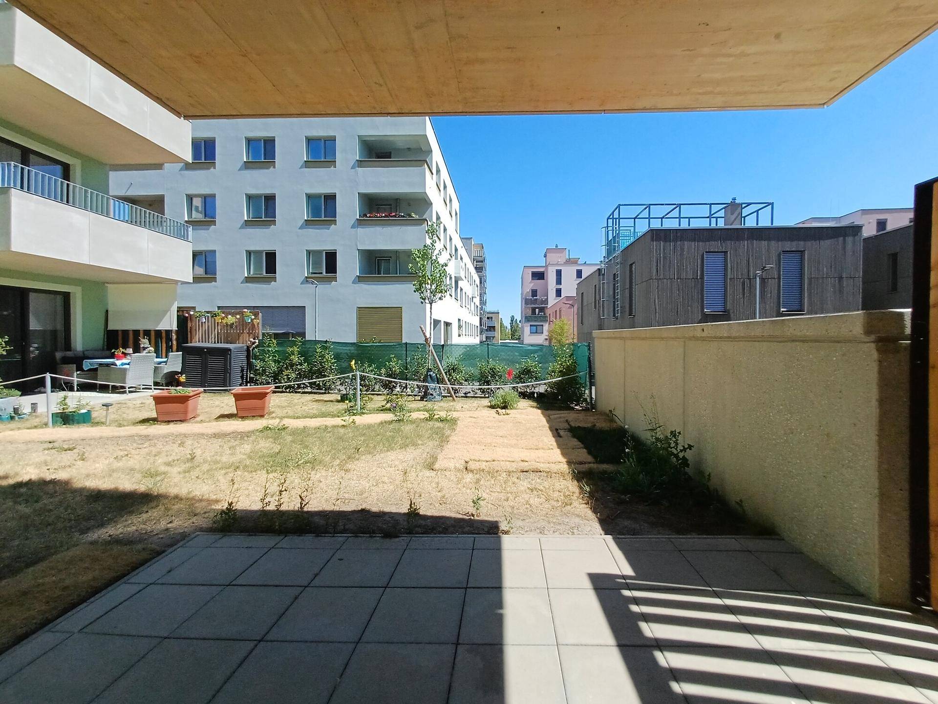 Eine sonnige Terrasse mit angrenzendem Gartenbereich und Blick auf die umliegenden Neubauten.