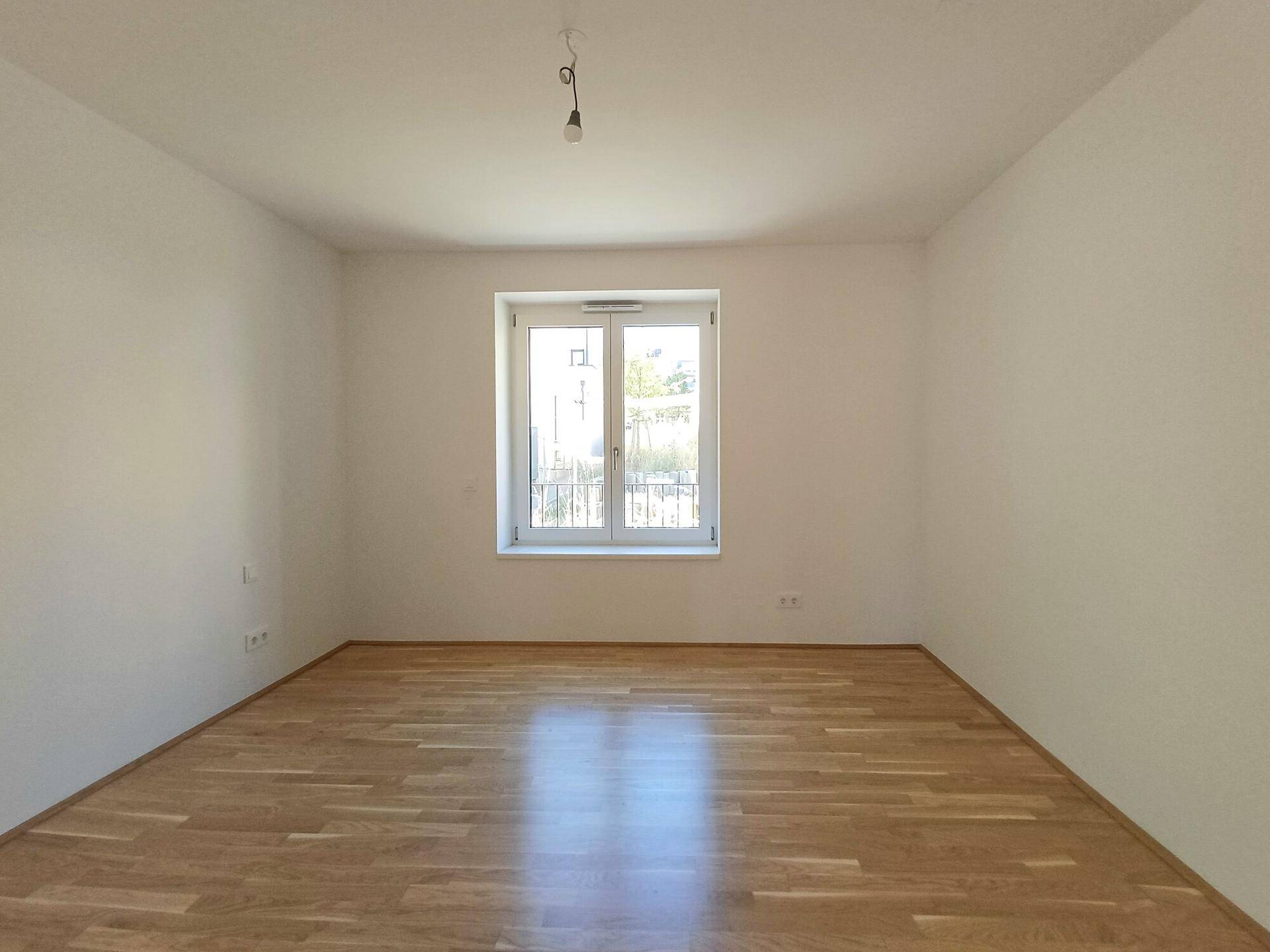Helles Zimmer mit Parkettboden und großem Fenster, ideal als Schlaf- oder Arbeitszimmer.