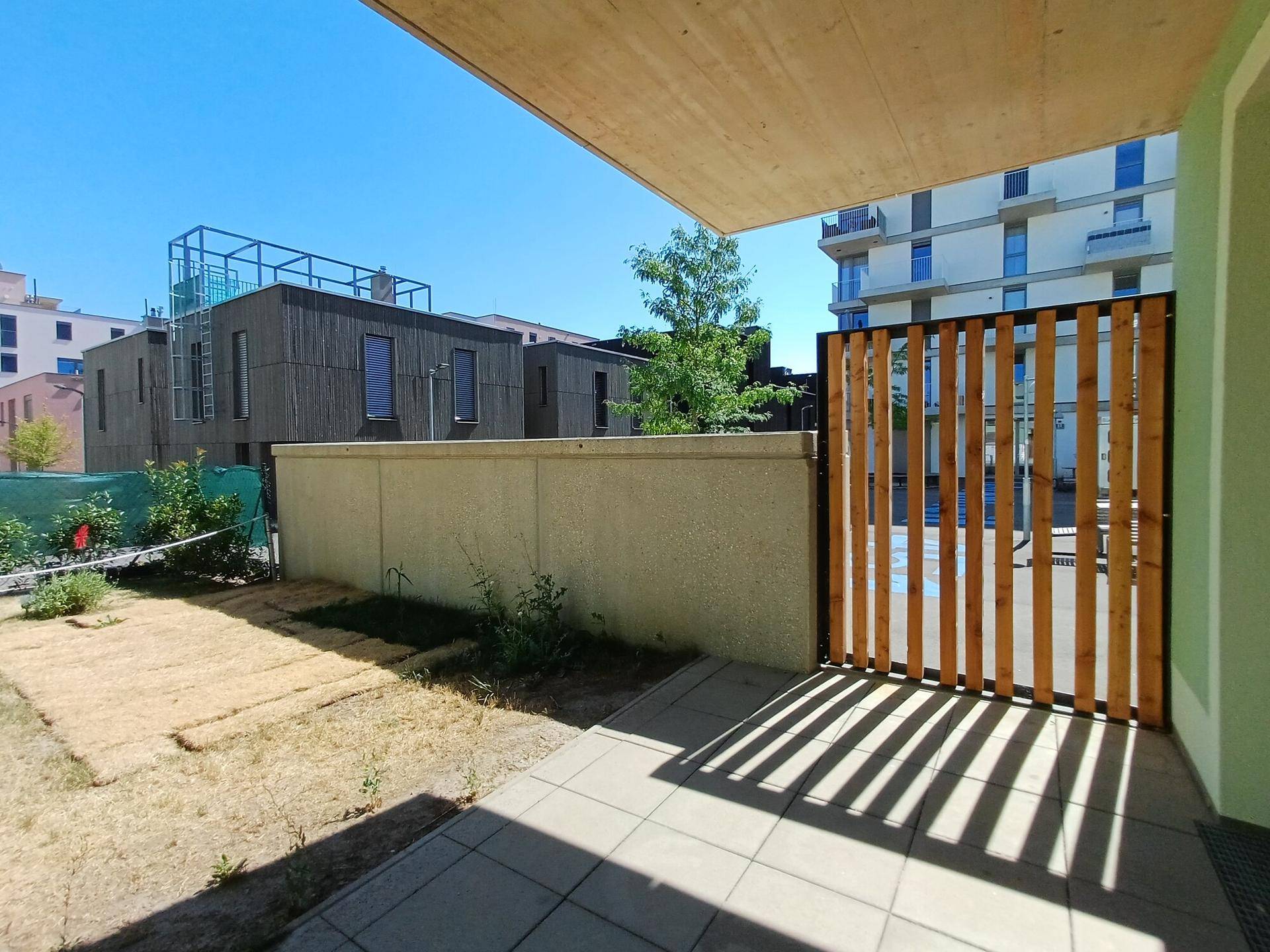 Eine gepflasterte Terrasse mit Holzzaun und Blick auf die moderne Architektur der Wohnanlage.