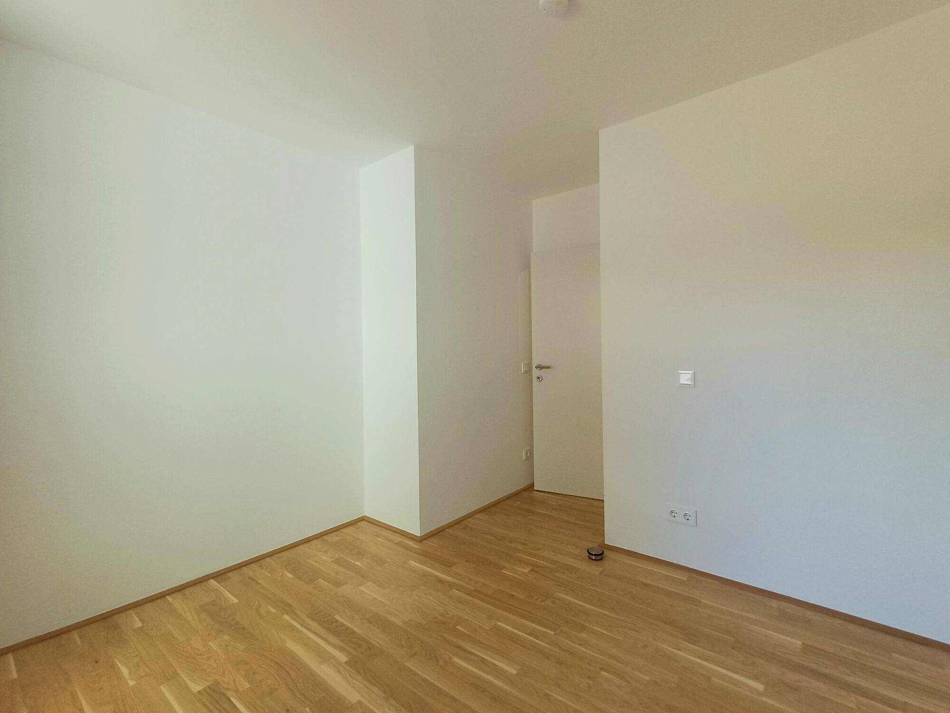 Leeres Zimmer mit Parkettboden und weißen Wänden, bereit für individuelle Gestaltung.
