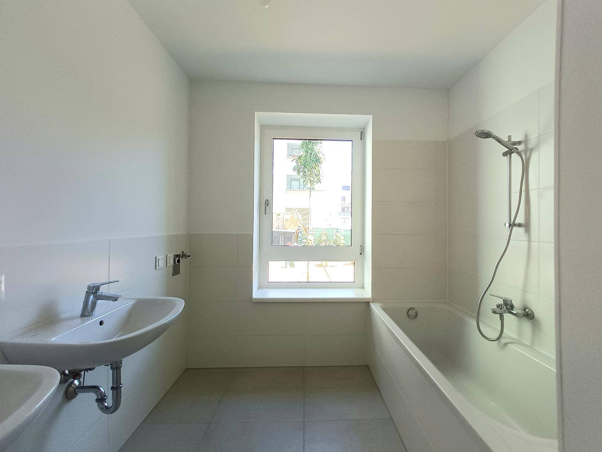 Modernes Badezimmer mit Badewanne, Waschbecken und Fenster für natürliche Belüftung.