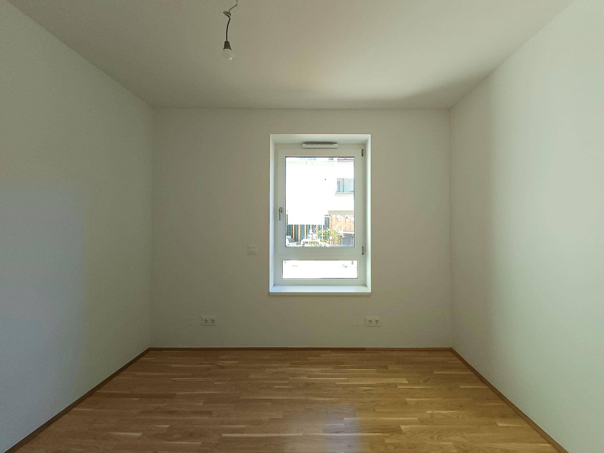 Freundliches Zimmer mit Parkettboden und Fenster, das viel Tageslicht hereinlässt.