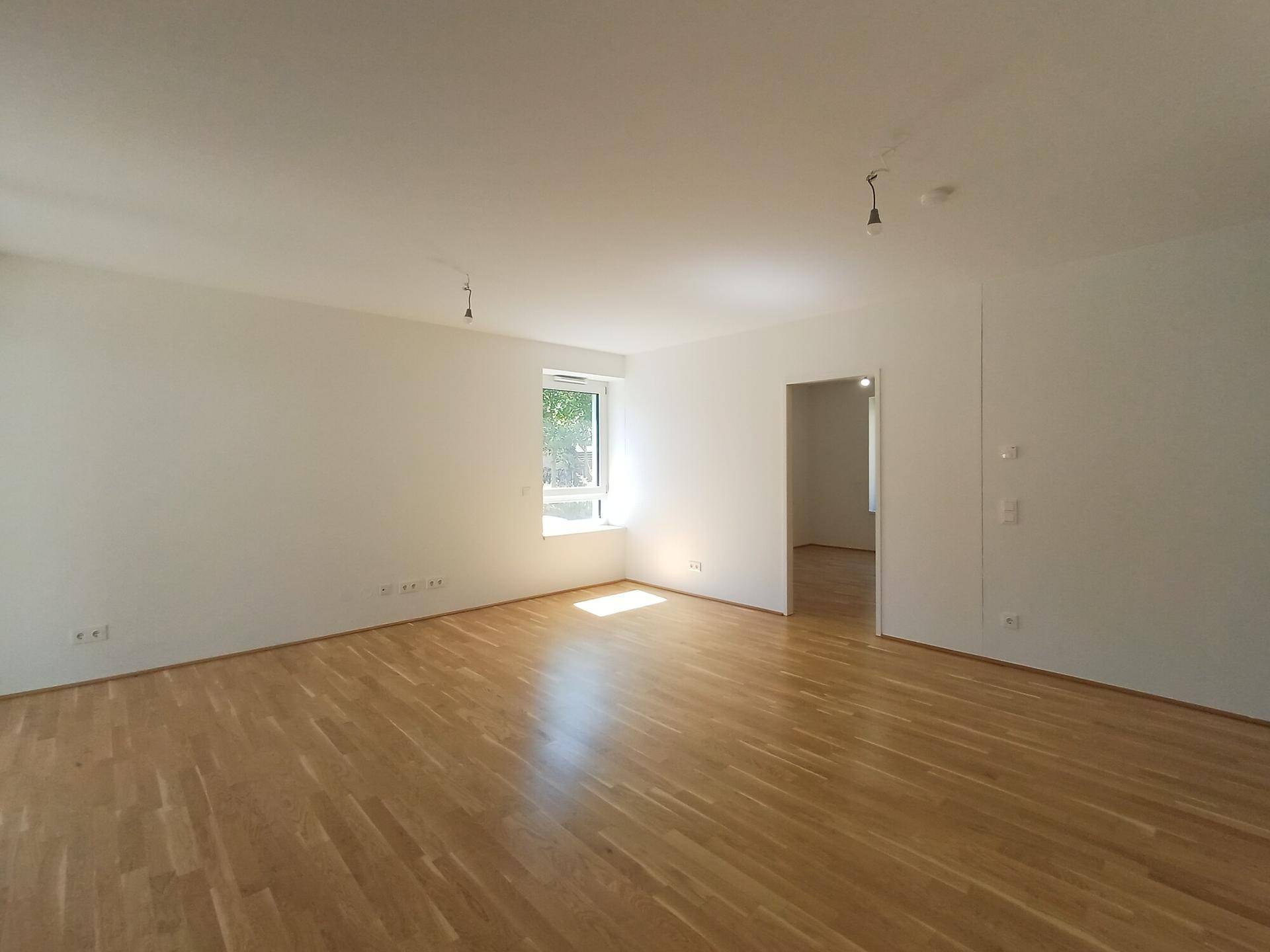 Geräumiges, helles Wohnzimmer mit Parkettboden und großem Fenster, bereit zur Einrichtung.