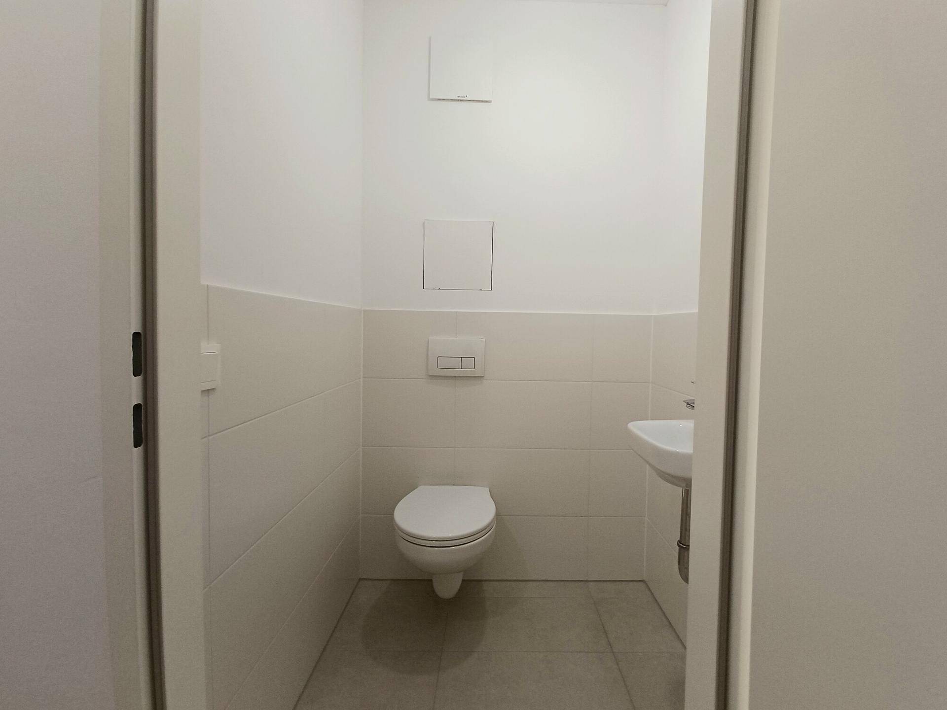 Separates Gäste-WC mit wandhängender Toilette, kleinem Waschbecken und Fliesenboden.