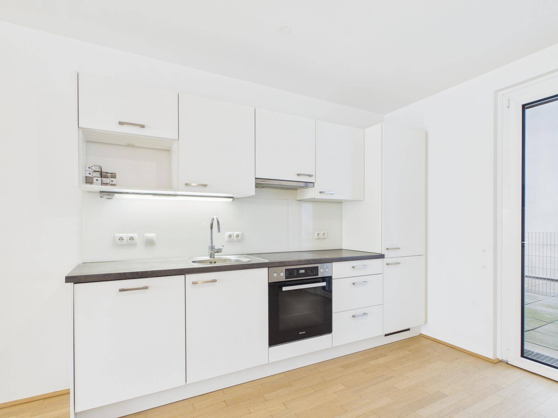 Moderne Einbauküche in Weiß mit dunkler Arbeitsplatte und integriertem Backofen.