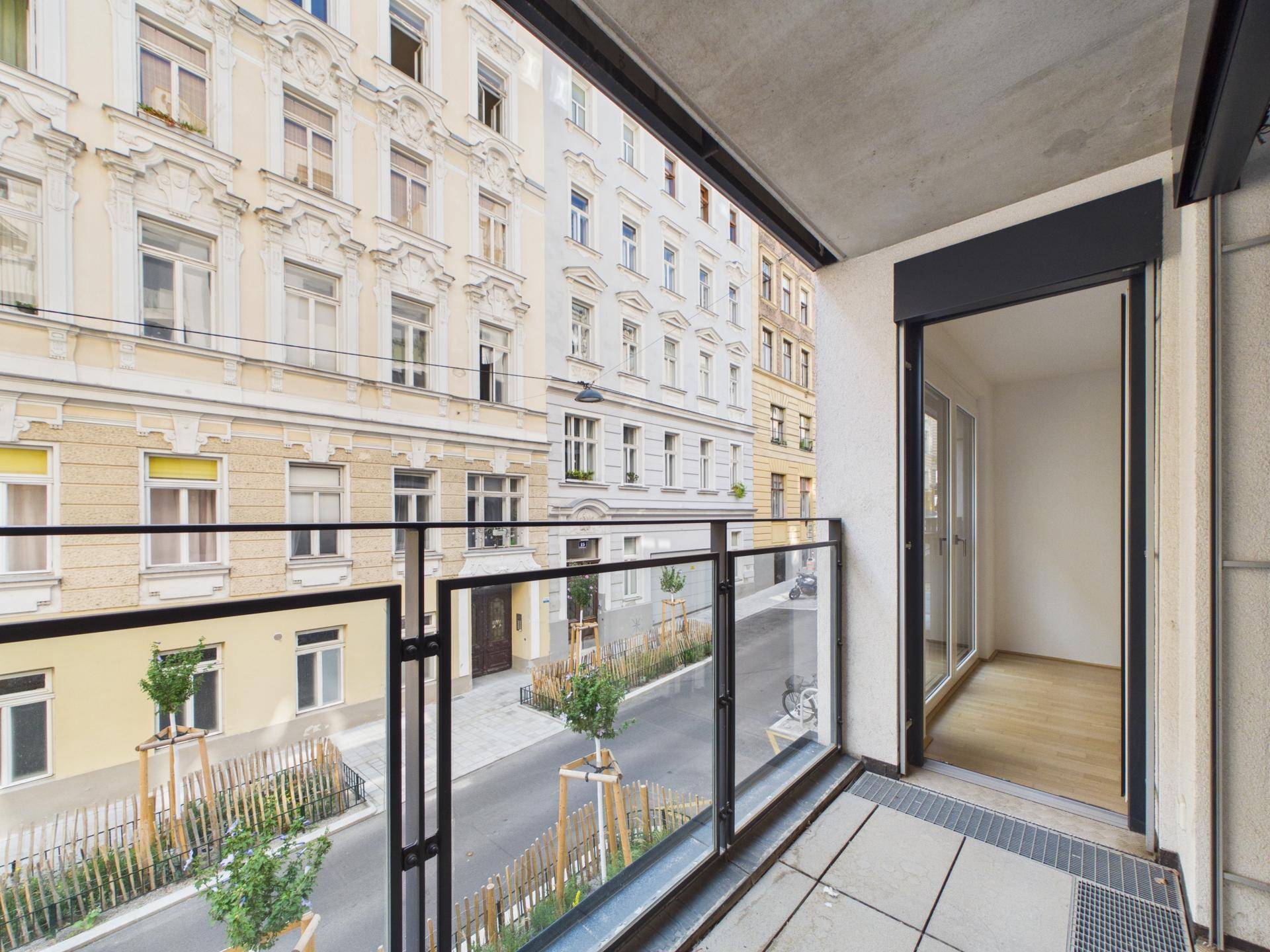 Moderner Balkon mit Glasgeländer und Blick auf die gegenüberliegende historische Fassade.