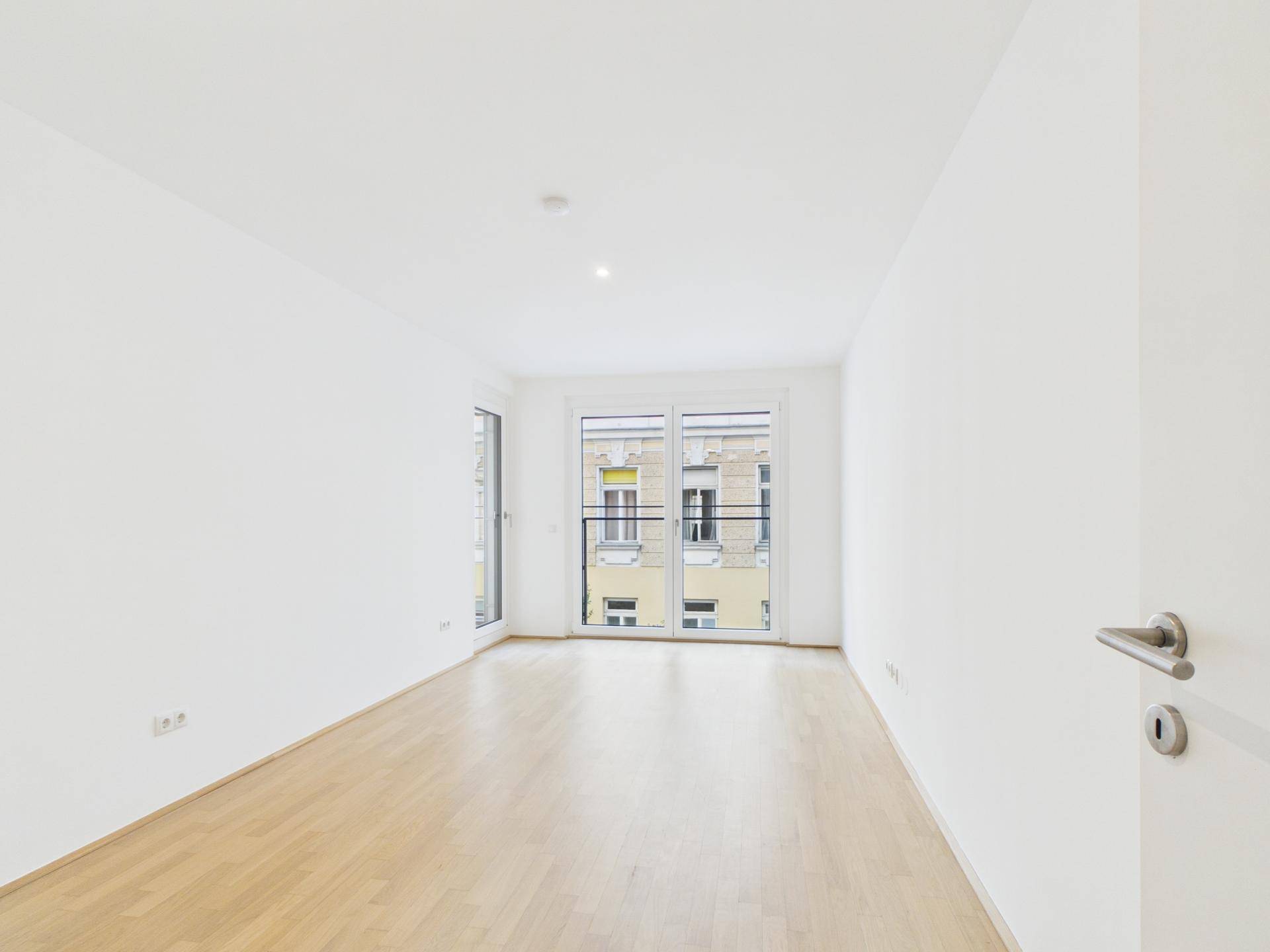 Heller Wohnraum mit Parkettboden und Zugang zu einem Balkon, der viel Tageslicht bietet.